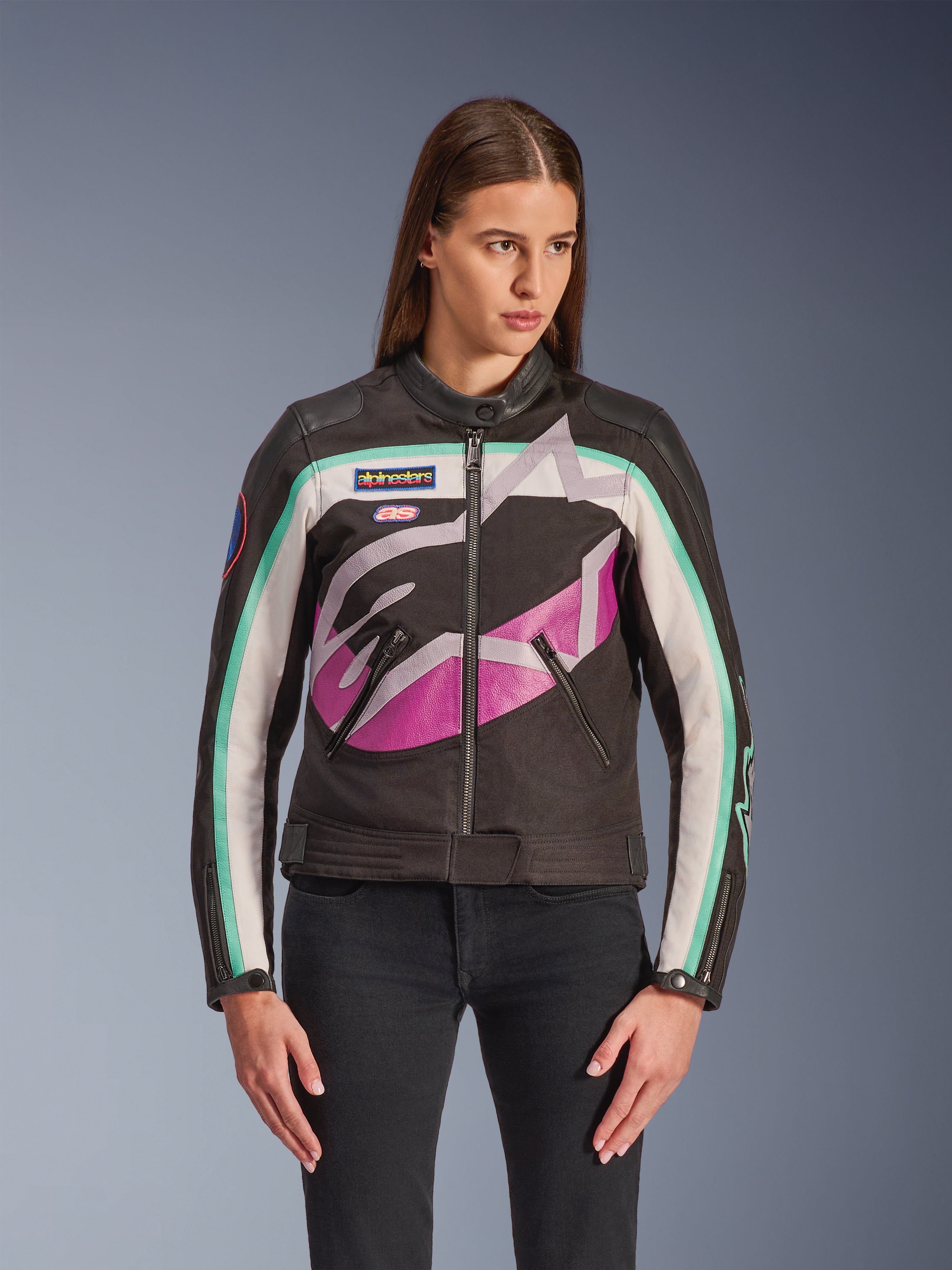 Alpinestars Idles damejakke, motorcykeljakke, sort med farveblok-design i råhvid, lilla og teal, vintage racing-inspireret stil med stort abstrakt logo på brystet, mærkede patches og lynlås foran, båret af model med sorte jeans