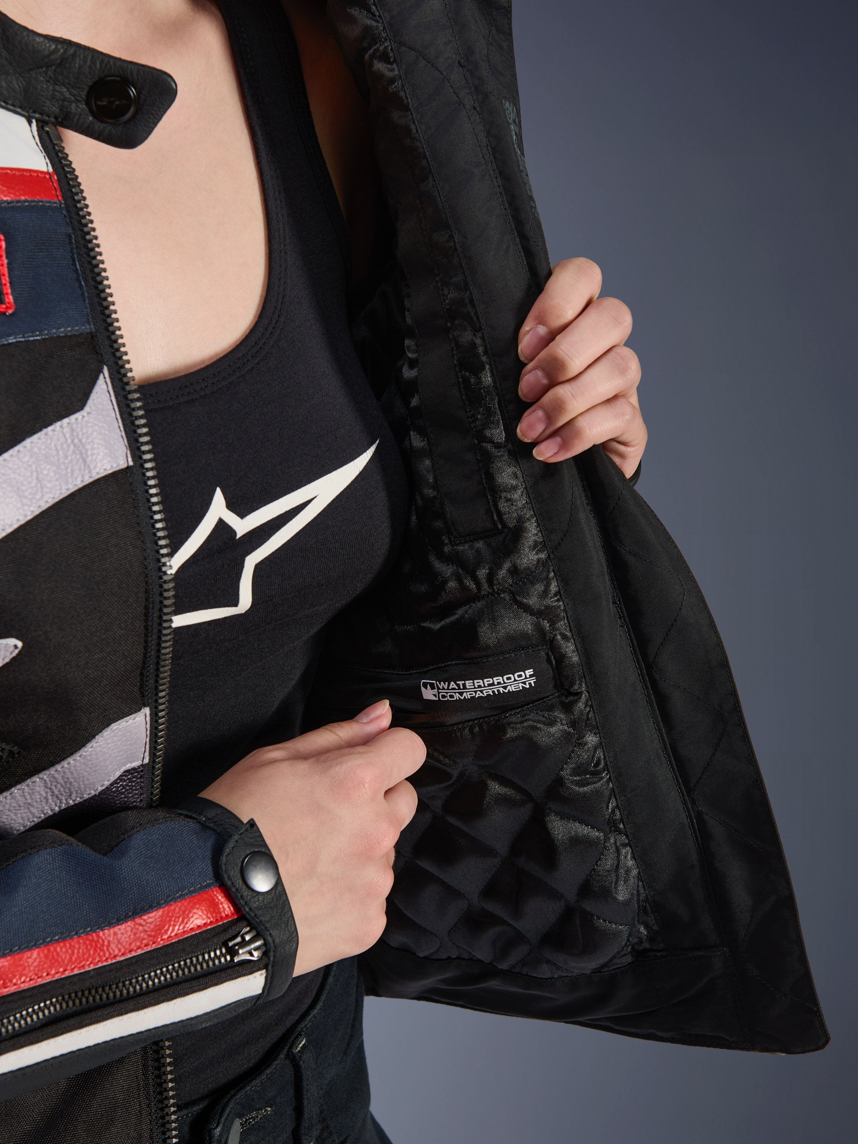 Alpinestars Idles damejakke, detalje af indersiden der viser sort quiltet for og markeret vandtæt rum, båret over en sort tanktop med logo, funktionelt motorcykeludstyr til kvinder