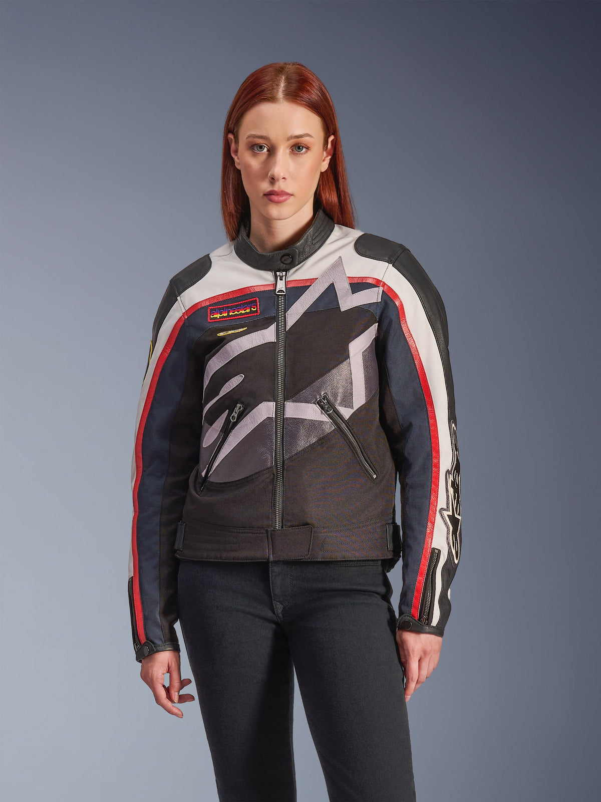 Alpinestars Idles-jakke, motorcykeljakke til damer, offwhite, flammerød og sort, med et stort stiliseret stjernelogo, vintage-inspirerede brystmærker, høj bikerkrave, lynlåslommer og stribede ærmer, båret af en kvindelig model med mørke jeans