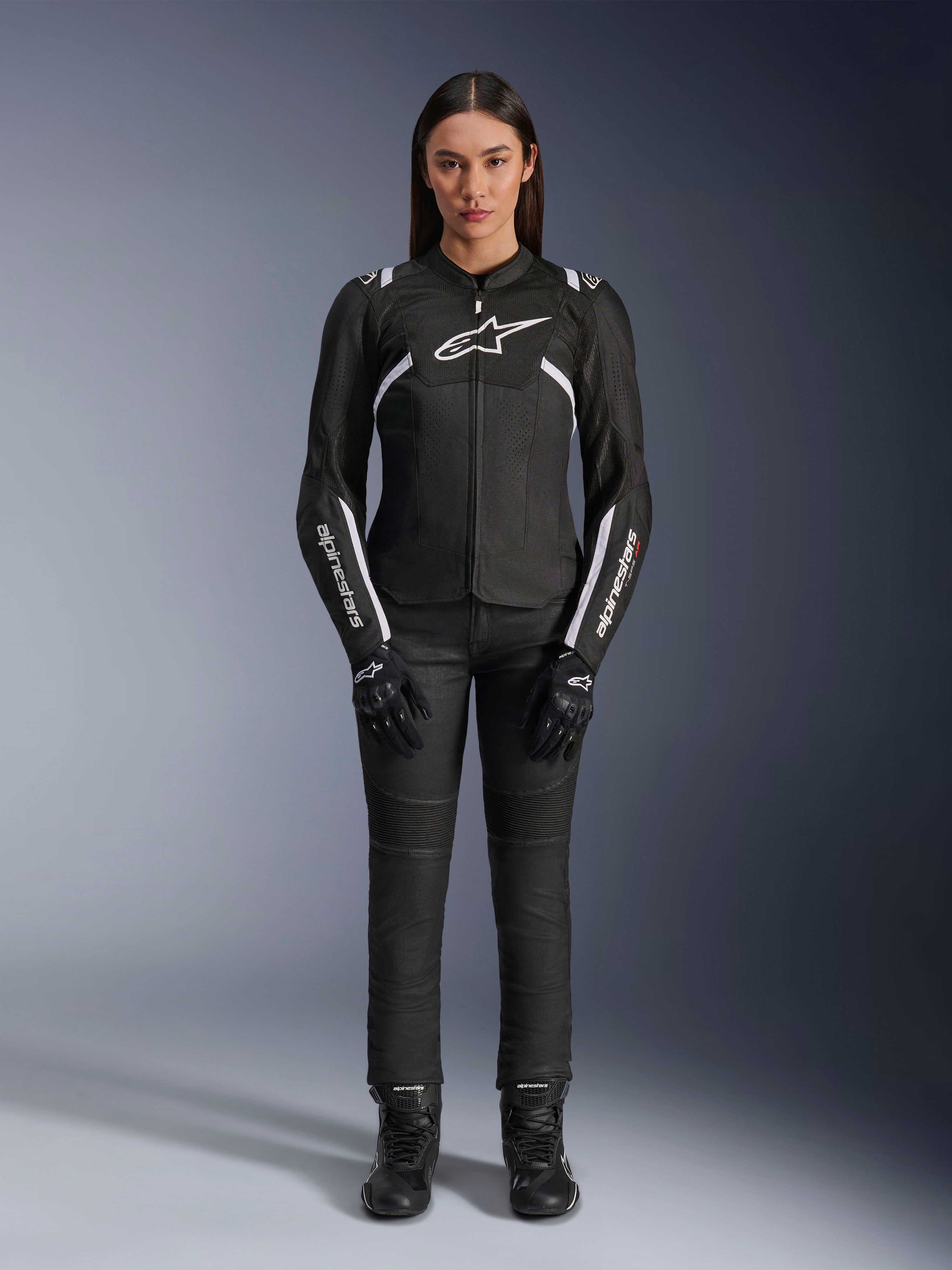 Alpinestars Stella T-Sps Air V2-jakke, motorcykeljakke til kvinder, sort og hvid, med mesh-paneler og hvide detaljer, båret med sorte bukser, handsker og støvler, atletisk pasform til bykørsel