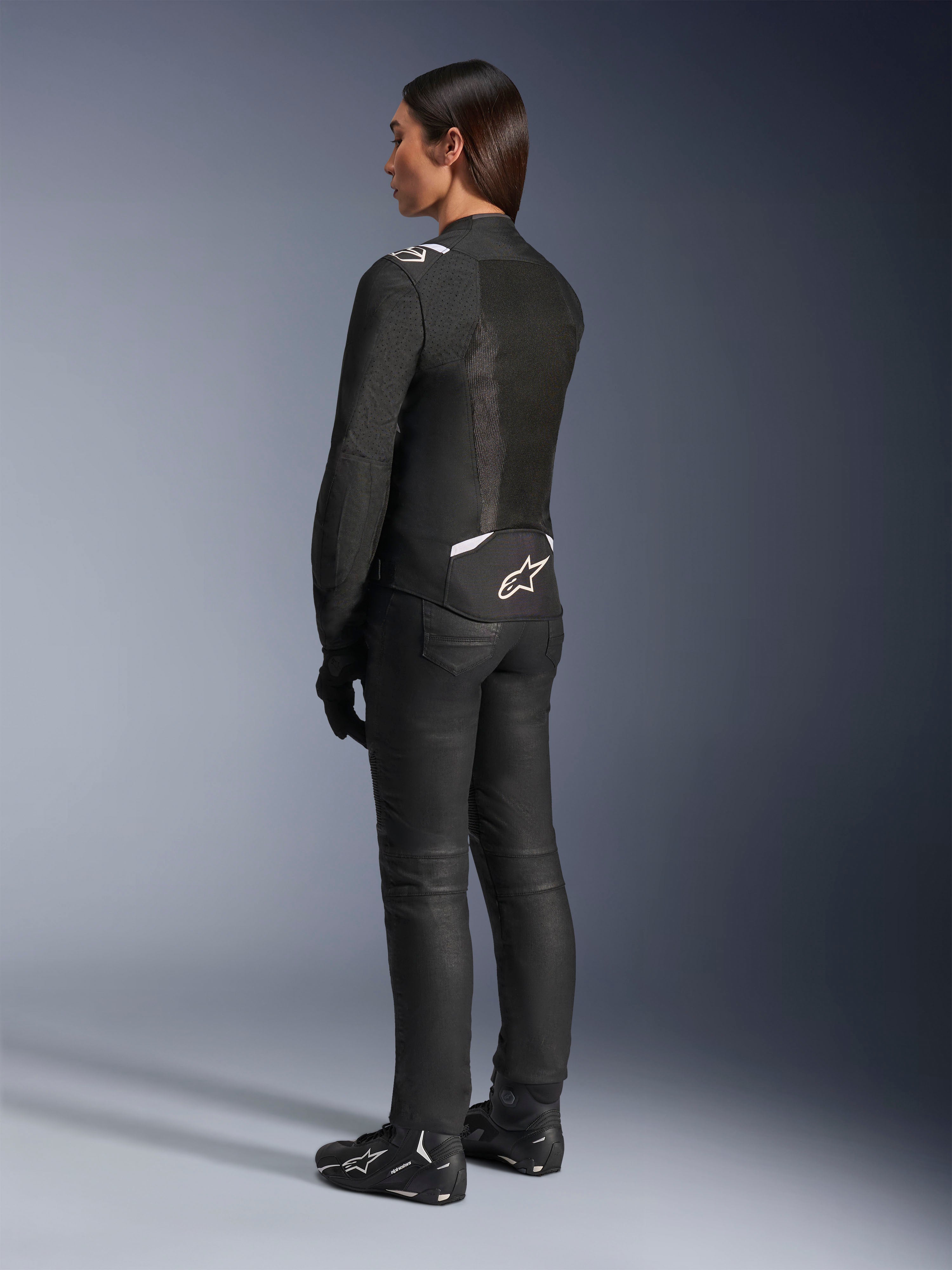 Alpinestars Stella T-Sps Air V2 jakke, sort og hvid, set bagfra med mesh-paneler og logo på den nederste del af ryggen, kombineret med sorte kørebukser og motorcykelsko, sportsligt tekstiludstyr til kvinder
