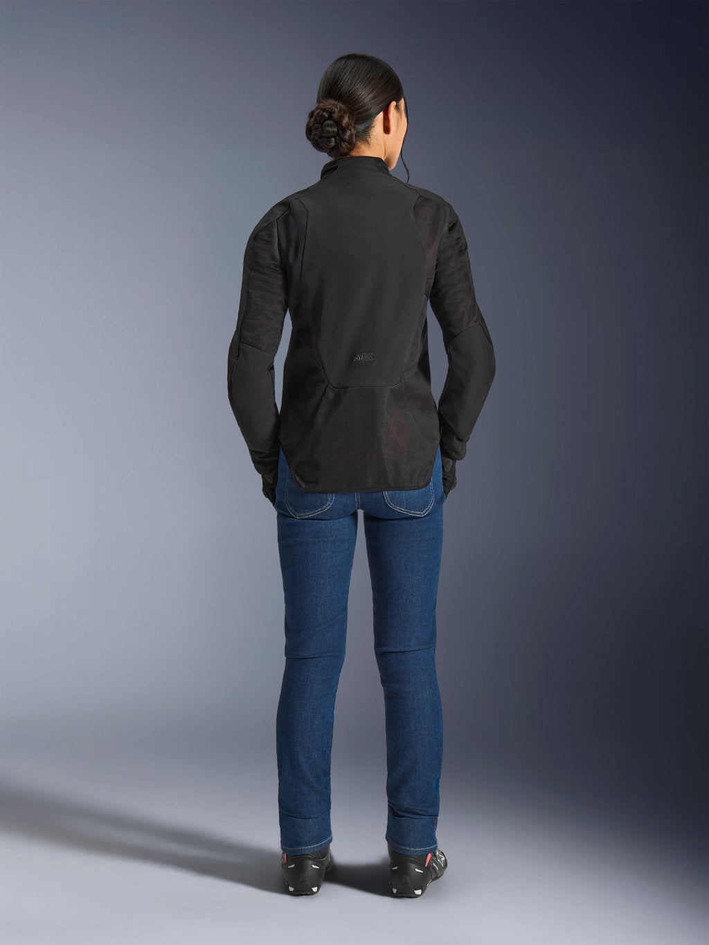 Alpinestars Stella Aeroshell Airflow jakke til kvinder, Black Anthracite, set bagfra på en model, letvægts softshell-chassis med laserperforerede mesh-paneler, forlænget bagprofil for dækning, sportslig pasform, kombineret med blå jeans