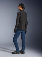 Kvinde iført Alpinestars Stella Aeroshell Airflow-jakke, Black Anthracite, trekvartvisning bagfra, der viser åndbare mesh-paneler og en forlænget bagprofil, kombineret med blå denim motorcykeljeans og sorte Alpinestars-sko