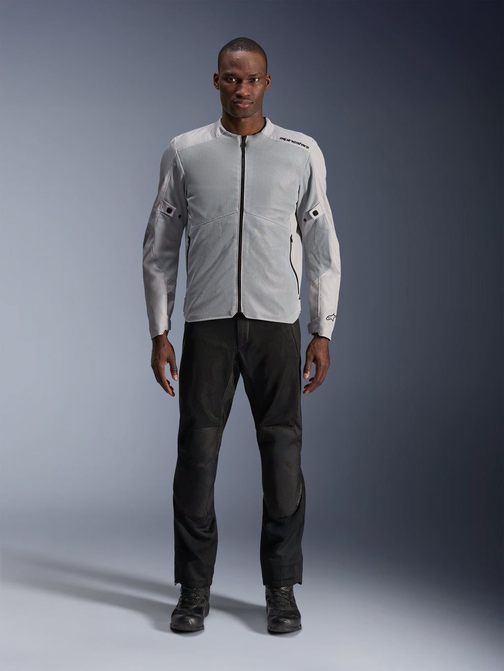 Alpinestars C-1 Air-jakke i sølv, urban tekstil-motorcykeljakke til mænd med ventilerede mesh-paneler, båret af en model med sorte kørebukser og sorte støvler, moderne pendlingsstil