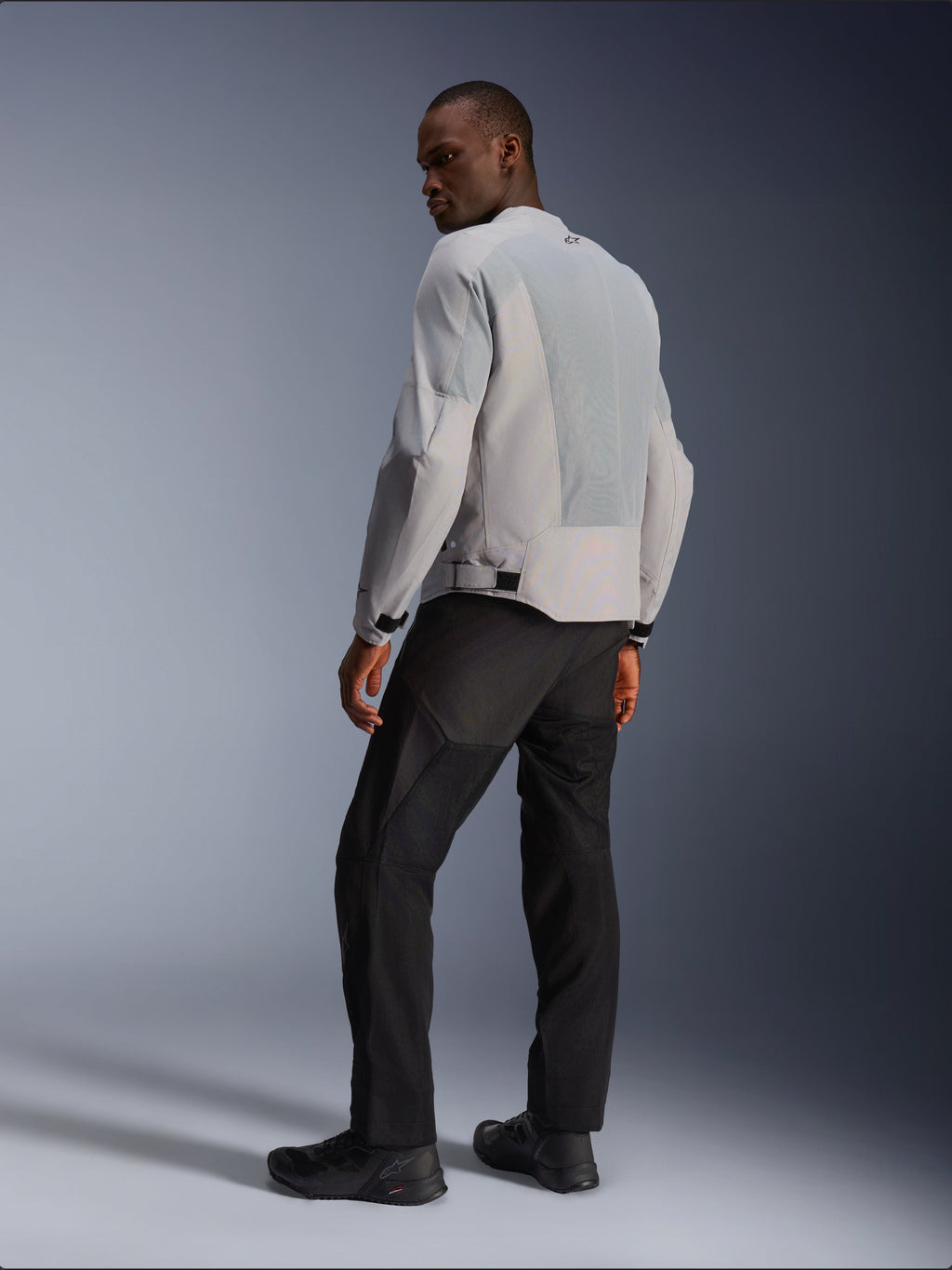 Alpinestars C-1 Air-jakke, sølv og grå, set bagfra på en model, med ventilerende tech mesh-paneler og reflekterende logoer, båret med sorte bukser og sko, urbant moderne motorcykeludstyr