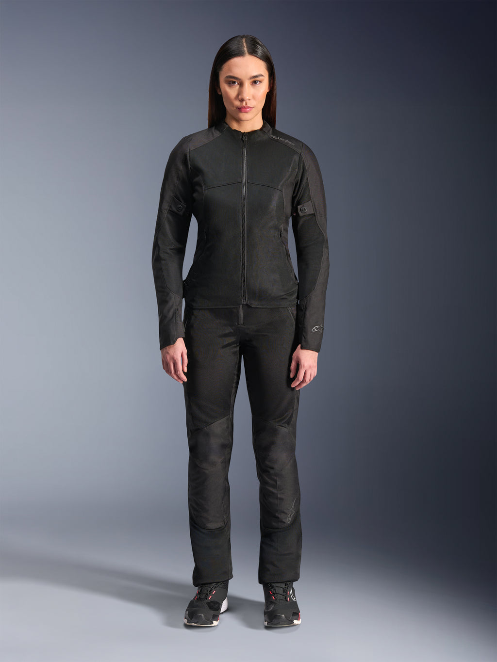 Kvinde iført Alpinestars Stella C-1 Air Jakke i sort, kombineret med matchende sorte tekstil-motorcykelbukser og køresko, med et stilrent urbant design med store mesh-paneler for luftgennemstrømning.