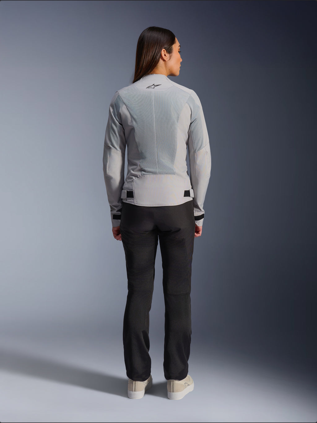 Alpinestars Stella C-1 Air-jakke til kvinder i sølv, set bagfra, med store tech mesh-paneler til ventilation og et reflekterende stjernelogo, kombineret med sorte motorcykelbukser og hvide sneakers, urbant moderne motorcykeludstyr