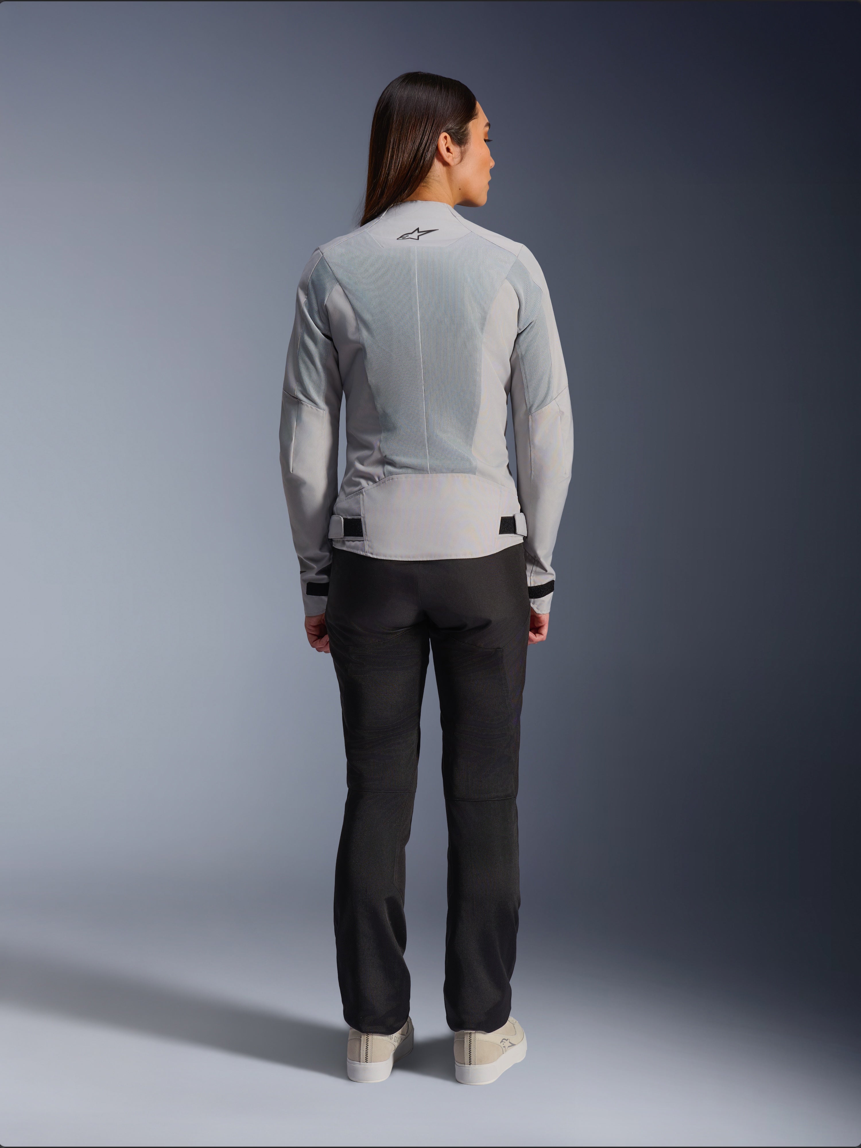 Alpinestars Stella C-1 Air-jakke til kvinder i sølv, set bagfra, med store tech mesh-paneler til ventilation og et reflekterende stjernelogo, kombineret med sorte motorcykelbukser og hvide sneakers, urbant moderne motorcykeludstyr