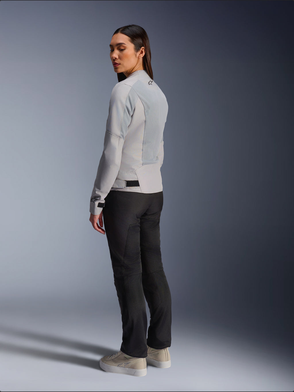 Kvinde iført Alpinestars Stella C-1 Air-jakke i Silver, ryg- og sidevisning der viser tech-mesh-paneler og reflekterende skulderlogo, kombineret med sorte motorcykelbukser og beige sneakers, moderne urban køreæstetik