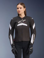 Alpinestars Stella T-GP Plus R V4-jakke, tekstil-motorcykeljakke til damer, sort og hvid, båret af en kvindelig model, med hvide stribedetaljer på ærmerne og brystet, Alpinestars-logo, sportspasform med lynlåslukning foran