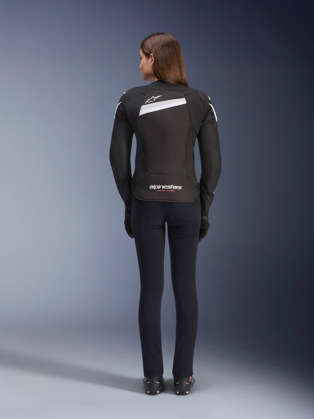 Alpinestars Stella T-GP Plus R V4 jakke, tekstil motorcykeljakke til damer, sort og hvid, set bagfra med hvide detaljer og logo-branding på ryggen, båret med sorte bukser, strømlinet sportspasform til landevejskørsel