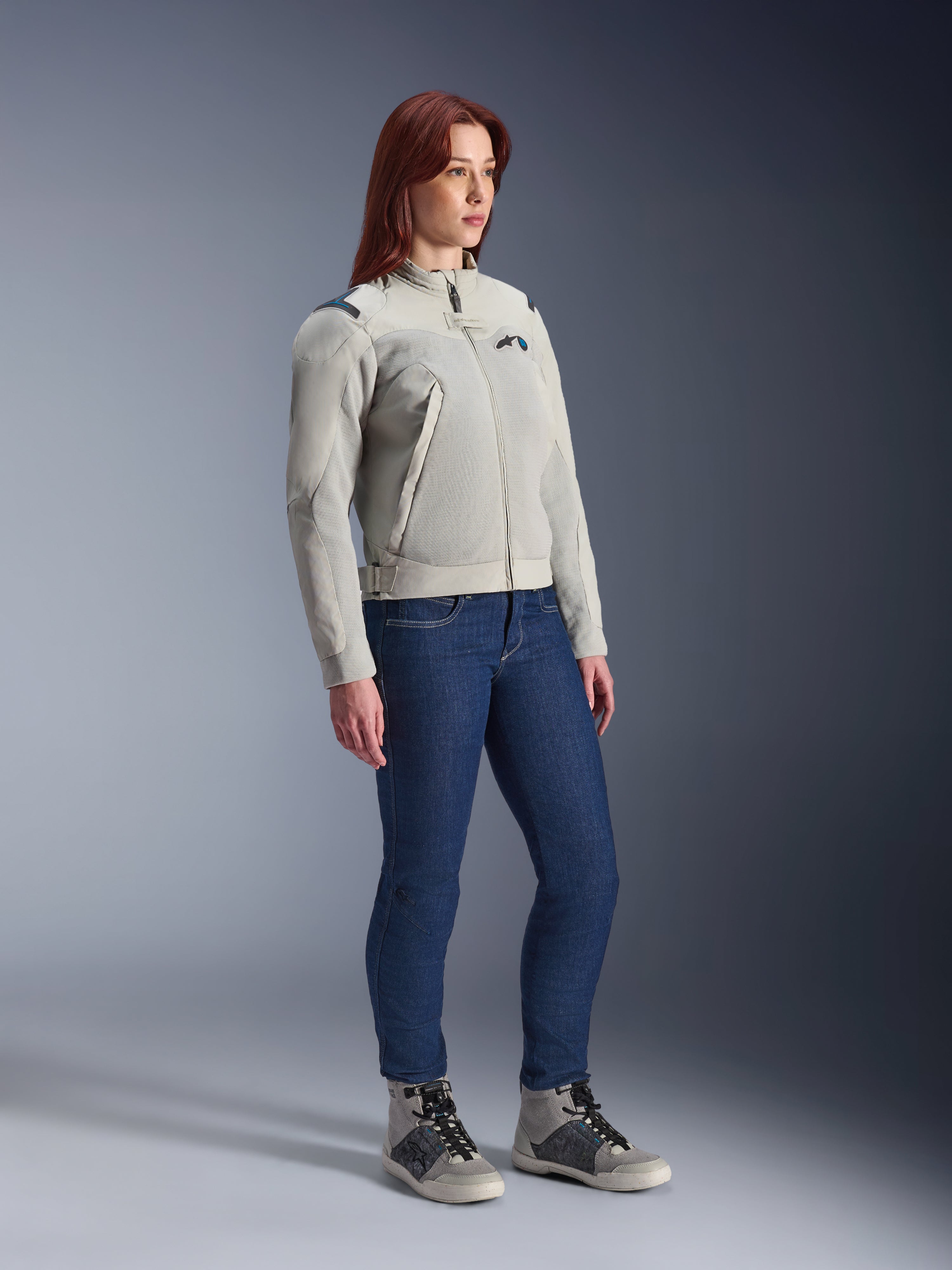 Kvinde iført Alpinestars Stella Circal-1 Air-jakken i Metal Gray og Methyl Blue, kombineret med blå jeans og afslappede køresko, der fremviser jakkens mesh-paneler og minimalistiske urbane design.