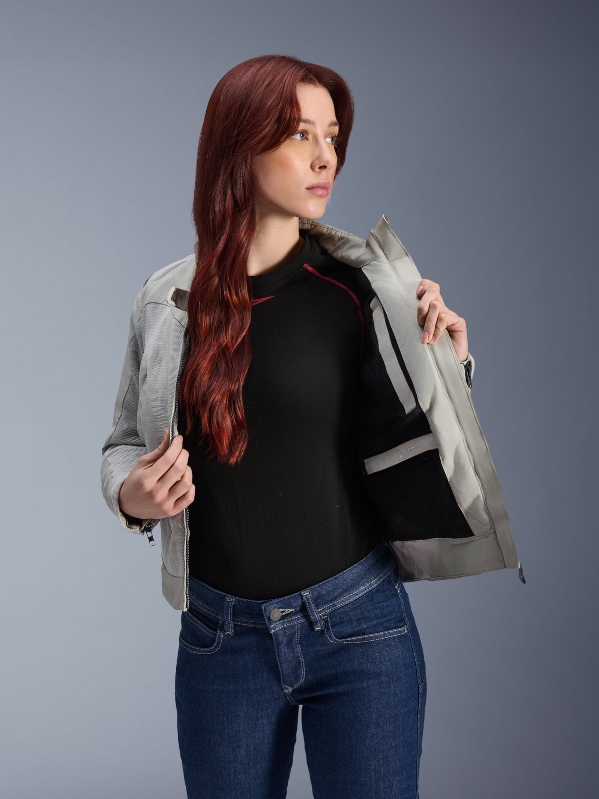 Alpinestars Stella Circal-1 Air-jakke i Metal Gray, kvindelig model åbner jakken for at vise det indvendige mesh-for og lommen, båret med blå jeans og en sort top, moderne urbant motorcykeludstyr.