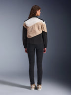 Alpinestars Stella Moshell-jakke, urban motorcykeljakke til kvinder, set bagfra, asymmetrisk design i Black Sand og Off White med stort grafisk omrids, båret med sorte slim-fit bukser og sandfarvede sneakers, urban køreudstyr