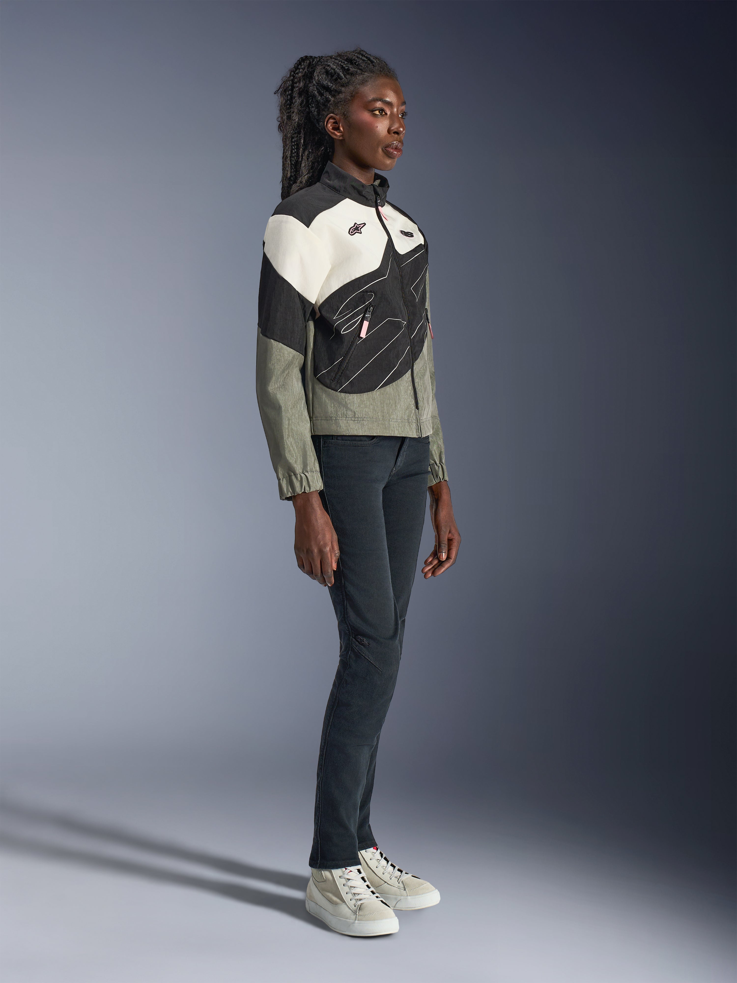Alpinestars Stella Moshell-jakke, urban motorcykeljakke til kvinder, grå, sort og råhvid med lyserøde detaljer, fuldlængde visning af kvindelig model iført mørke bukser og sneakers, moderne streetwear-inspireret design til bykørsel