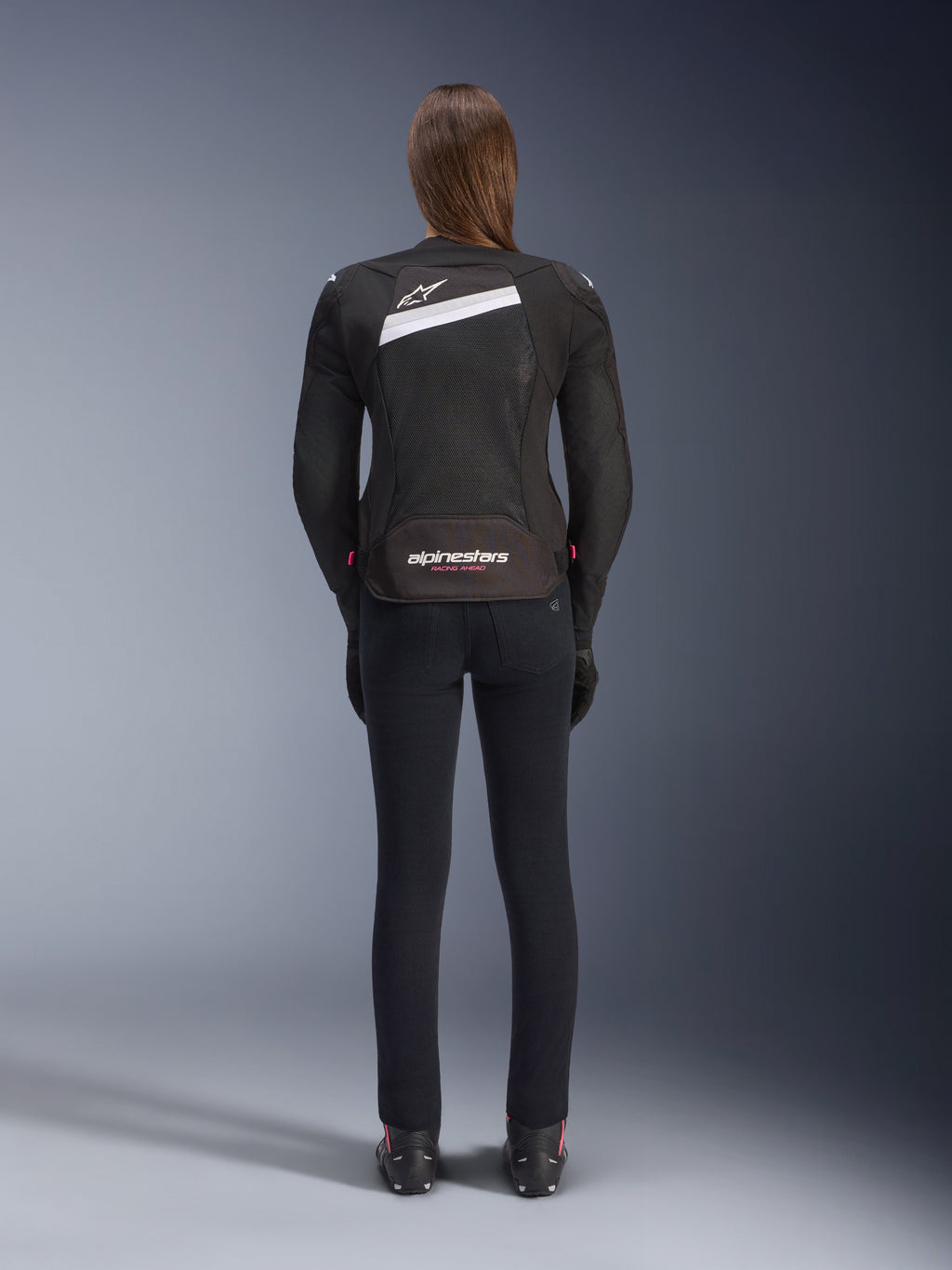 Alpinestars Stella T-GP Plus R V4 Airflow-jakke, sort og hvid, set bagfra med omfattende mesh-ventilationspaneler og Alpinestars-branding, båret af en kvindelig motorcyklist med sorte slim-fit motorcykelbukser og støvler, sport-fit tekstiludstyr til kvinder