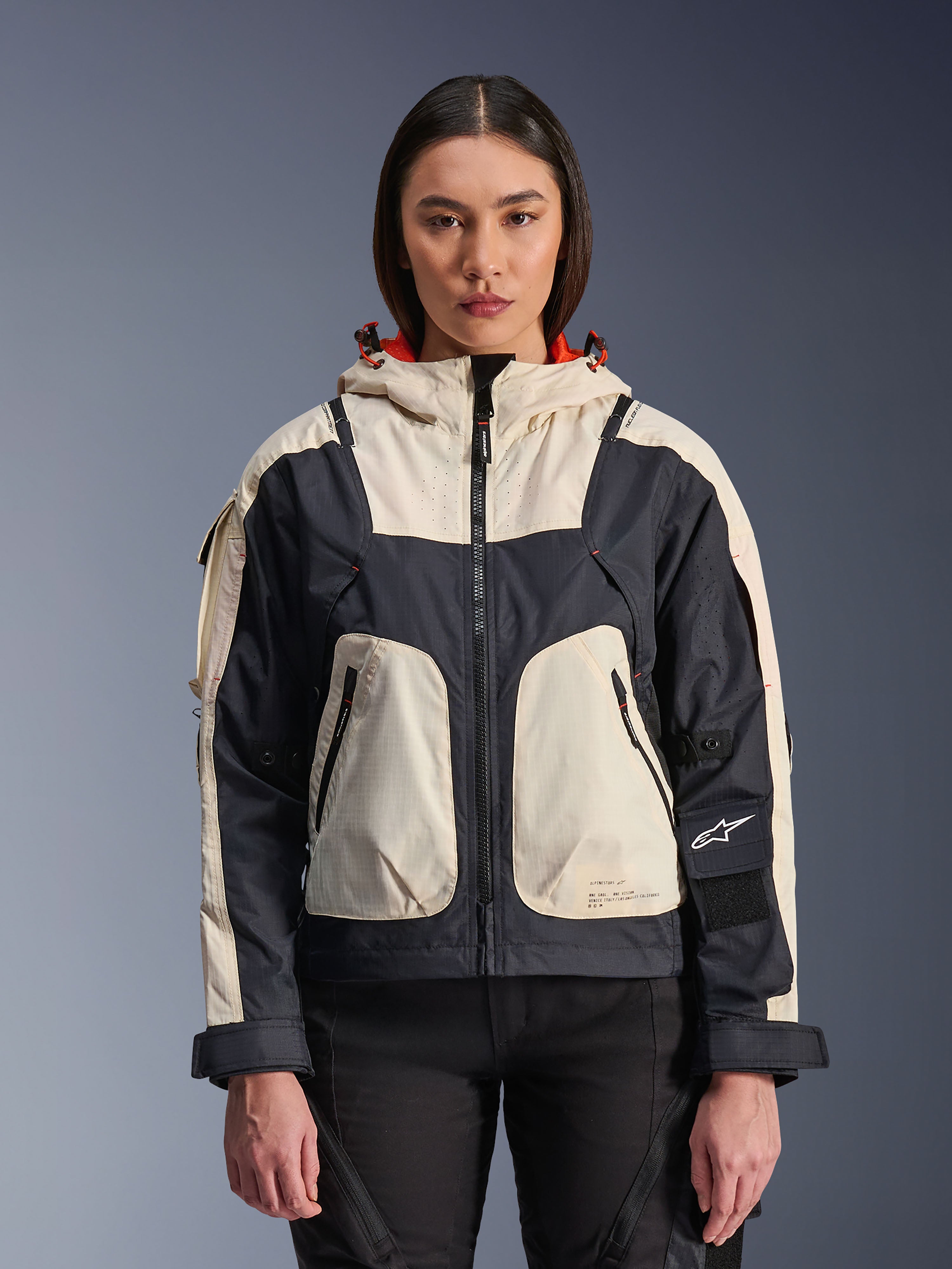 Alpinestars Molly Air jakke, urban motorcykeljakke til damer, Black Almond, set forfra på en model, med creme- og sorte ripstop-paneler, hætte med orange for, lynlåslukning foran og store utility-lommer, moderne streetwear-inspireret motorcykeludstyr