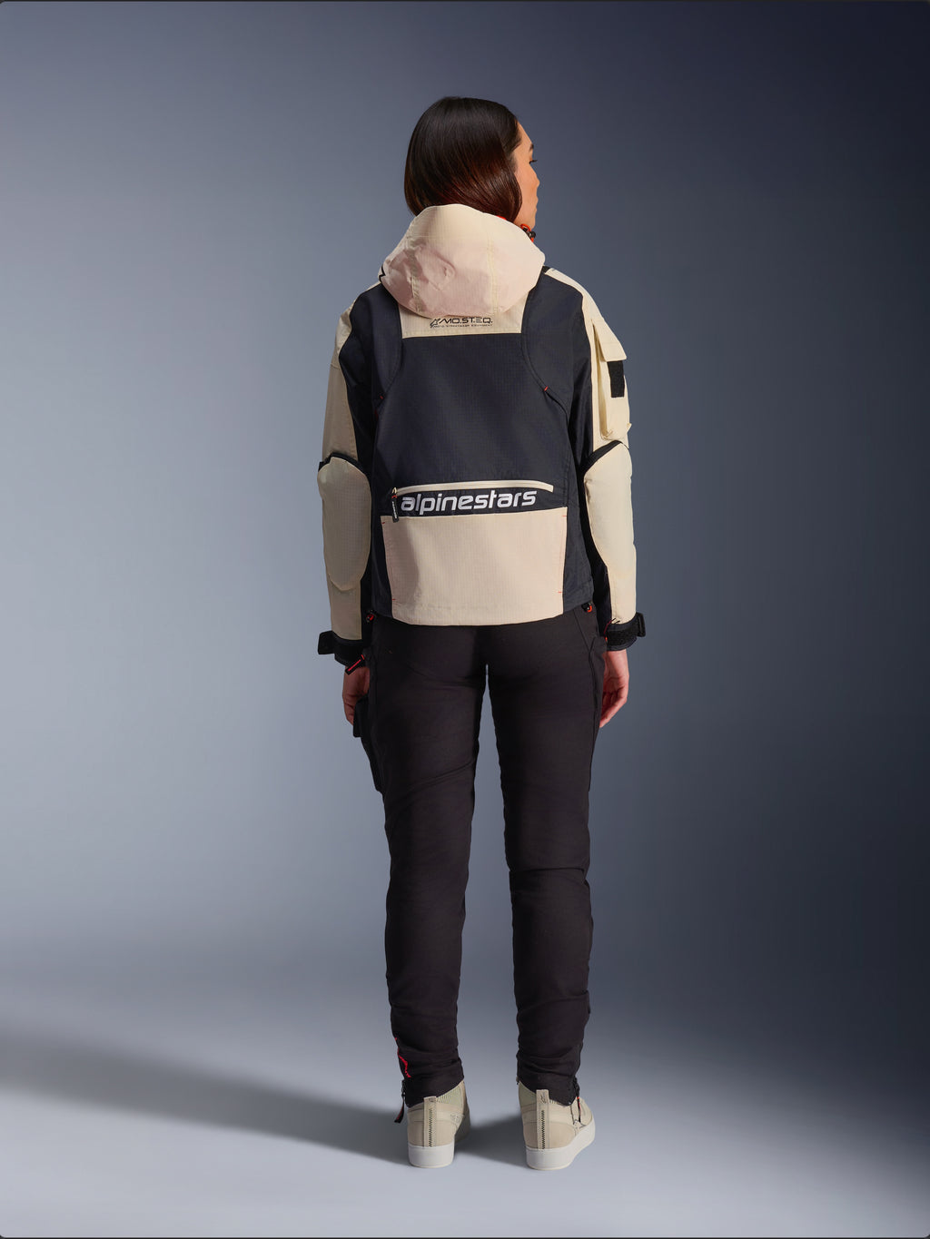 Alpinestars Molly Air Jakke, motorcykeljakke til damer, Black Almond, set bagfra, der viser hætten og det store logo på ryggen, utility-inspireret ripstop-design, stylet med sorte motorcykelbukser.