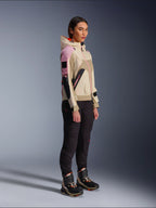 Kvindelig model iført Alpinestars Molly Air-jakke i Sand Pink Almond, kombineret med mørke tekniske bukser og high-top kørestøvler, urban motorcykeljakke med hætte og flerfarvede paneler, moderne streetwear-inspireret design