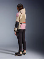 Alpinestars Molly Air Jakke, urban motorcykelstil med hætte, i farven Sand Pink Almond med et flerfarvet beige og lyserødt design, vist fra siden bagfra med sorte kørebukser og matchende tekniske støvler.