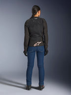 Kvindelig kører set bagfra iført Alpinestars Stella SMX Air-jakke i sort, kombineret med blå denim-kørebukser og sorte handsker, med ventileret tekstildesign, hvidt stjernelogo på lænden og Tech-Air Ready-branding, designet til sportskørsel i varmt vejr
