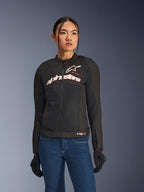 Kvinde iført Alpinestars Stella SMX Air jakke, sort hvid rød fluo, tekstil motorcykeljakke med ventileret mesh og hvidt brystlogo, stylet med blå jeans og sorte kørehandsker, feminin pasform til sportskørsel