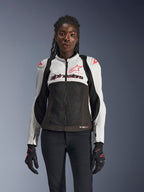 Alpinestars Stella SMX Air jakke til kvinder, Ice Gray, sort og Coral Fluo, med mesh-konstruktion og perforerede paneler, båret af en kvindelig model med sorte motorcykelhandsker og bukser, set forfra
