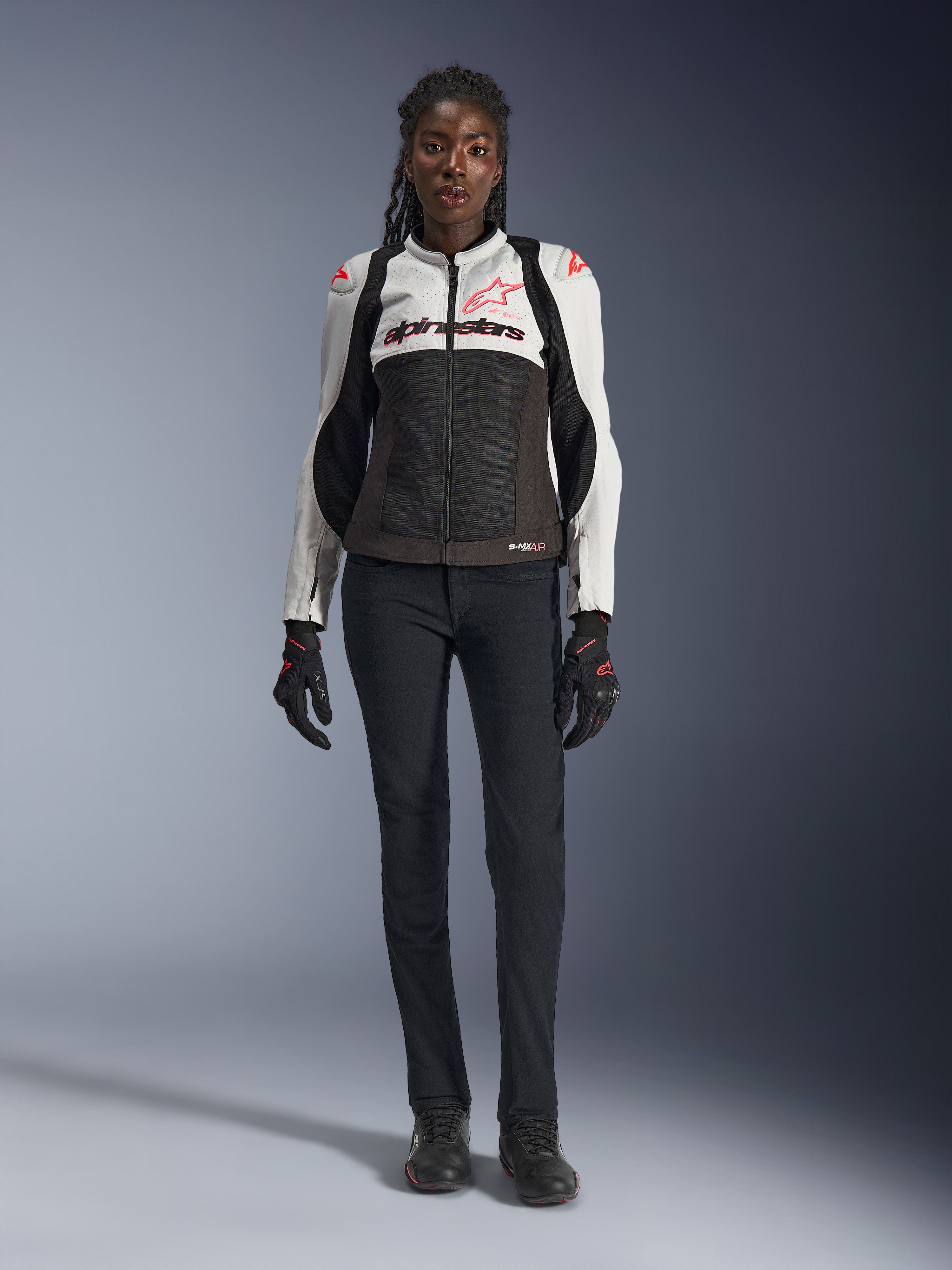 Alpinestars Stella SMX Air Jakke, Ice Gray Black og Coral Fluo, båret af en kvindelig model med sorte motorcykelbukser og handsker, med mesh-chassis og beskyttende skuldersliders, sportsmotorcykeludstyr til kvinder