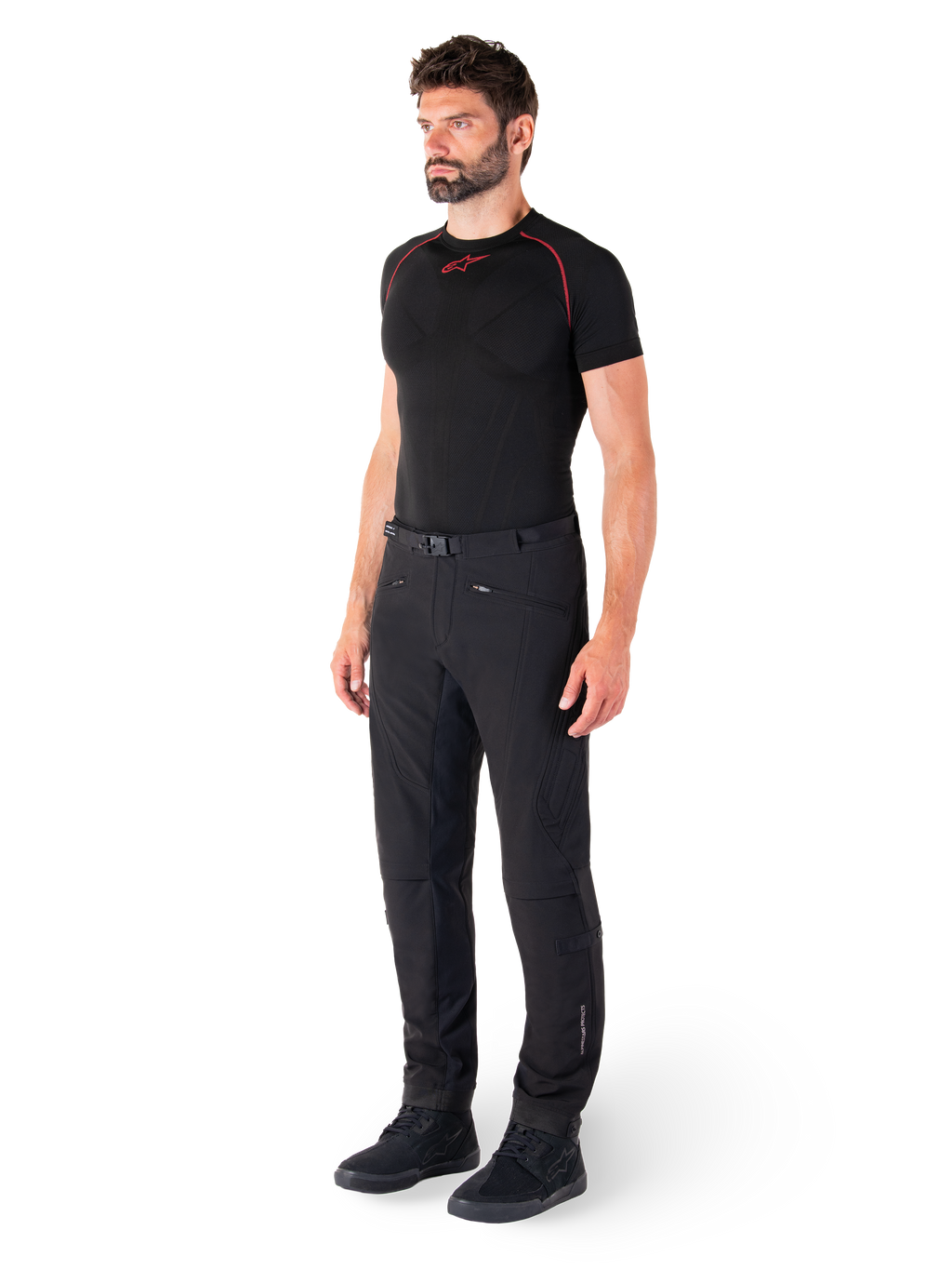 Alpinestars Alden bukser, urbane motorcykelbukser, sorte, regular fit softshell-tekstil, båret af en model med et sort basislag og køresko, med taljebælte med magnetisk lukning og lynlåslommer.