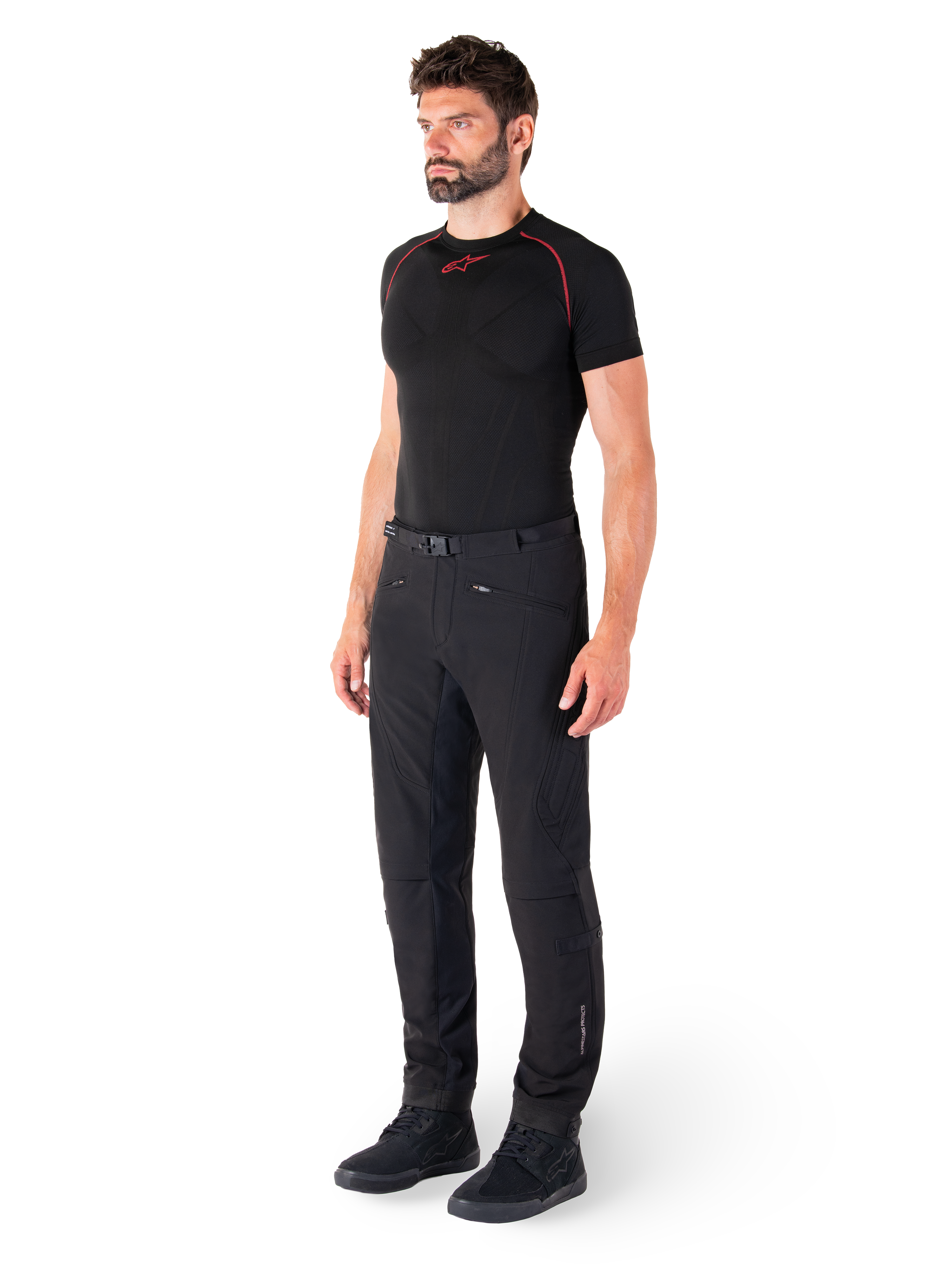 Alpinestars Alden bukser, urbane motorcykelbukser, sorte, regular fit softshell-tekstil, båret af en model med et sort basislag og køresko, med taljebælte med magnetisk lukning og lynlåslommer.