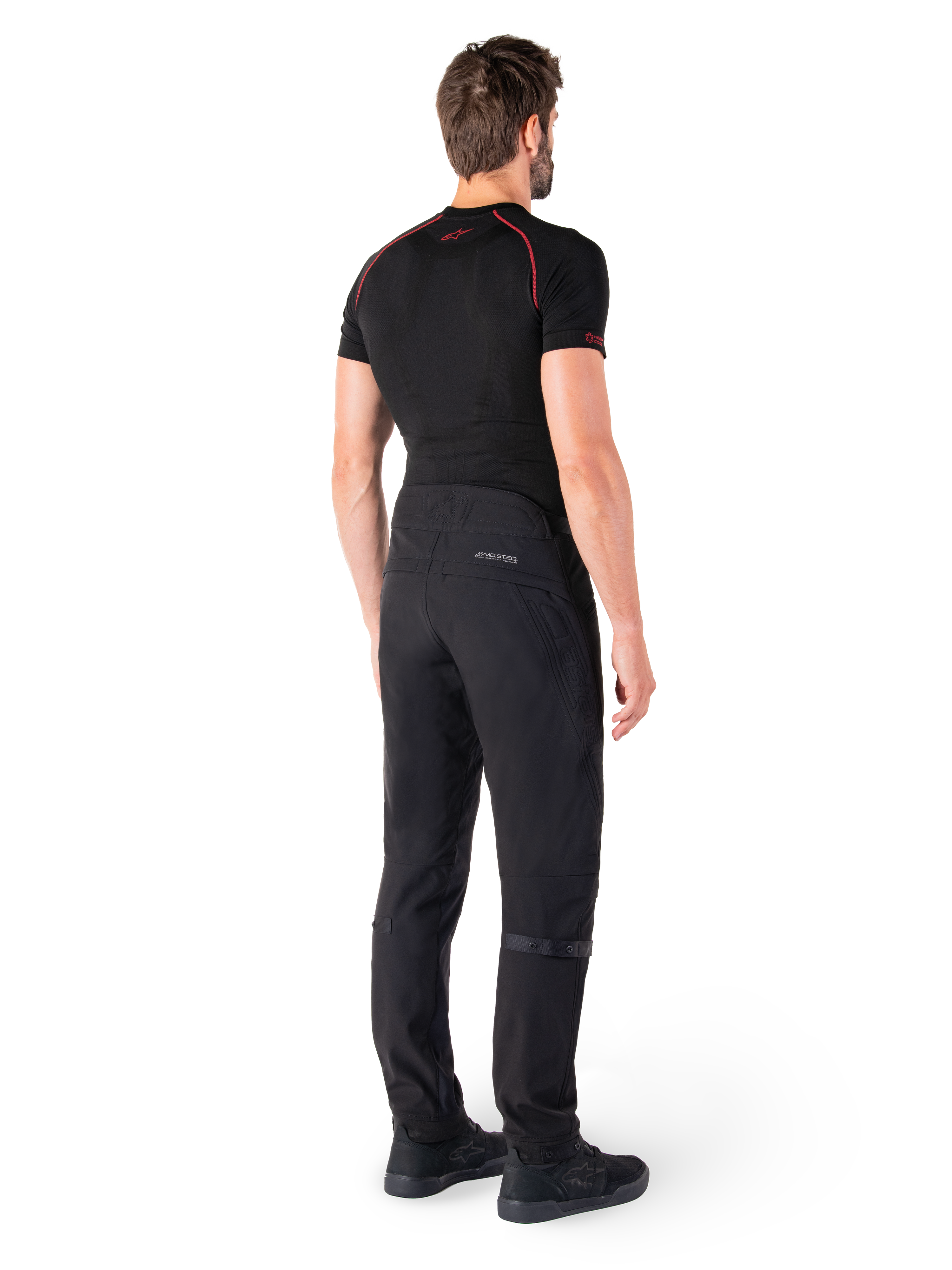 Alpinestars Alden bukser, sorte, urbane motorcykelbukser vist bagfra på en model, båret med et sort kortærmet baselayer og sorte køresko, med quiltede detaljer og reflekterende MO.ST.EQ.-branding på bagstykket.