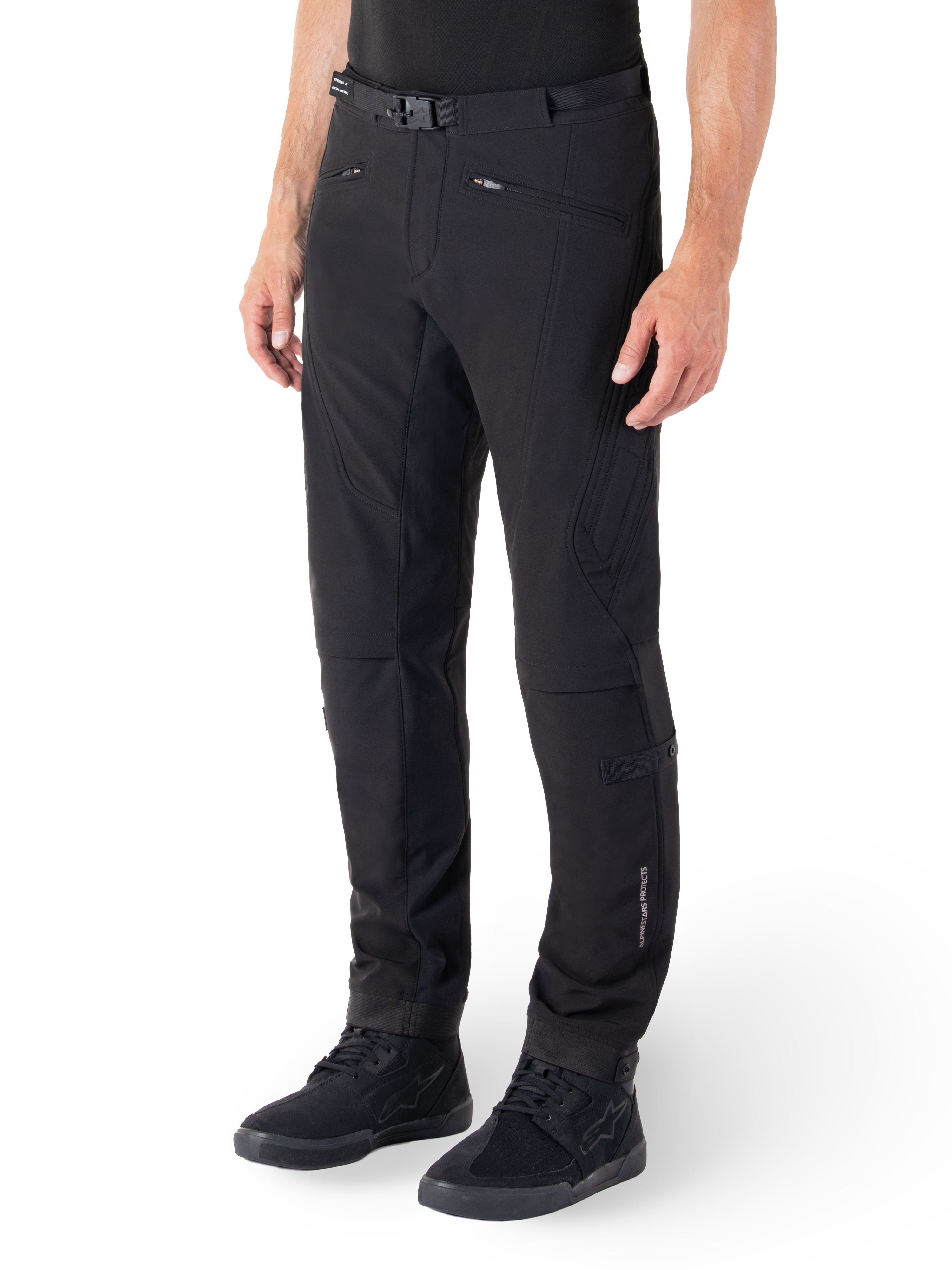 Alpinestars Alden bukser, urbane motorcykelbukser, sort, teknisk softshell-materiale med regular fit, med magnetisk taljespænde, quiltede sidepaneler, lynlåslommer og subtil branding på underbenet, vist med sorte køresko