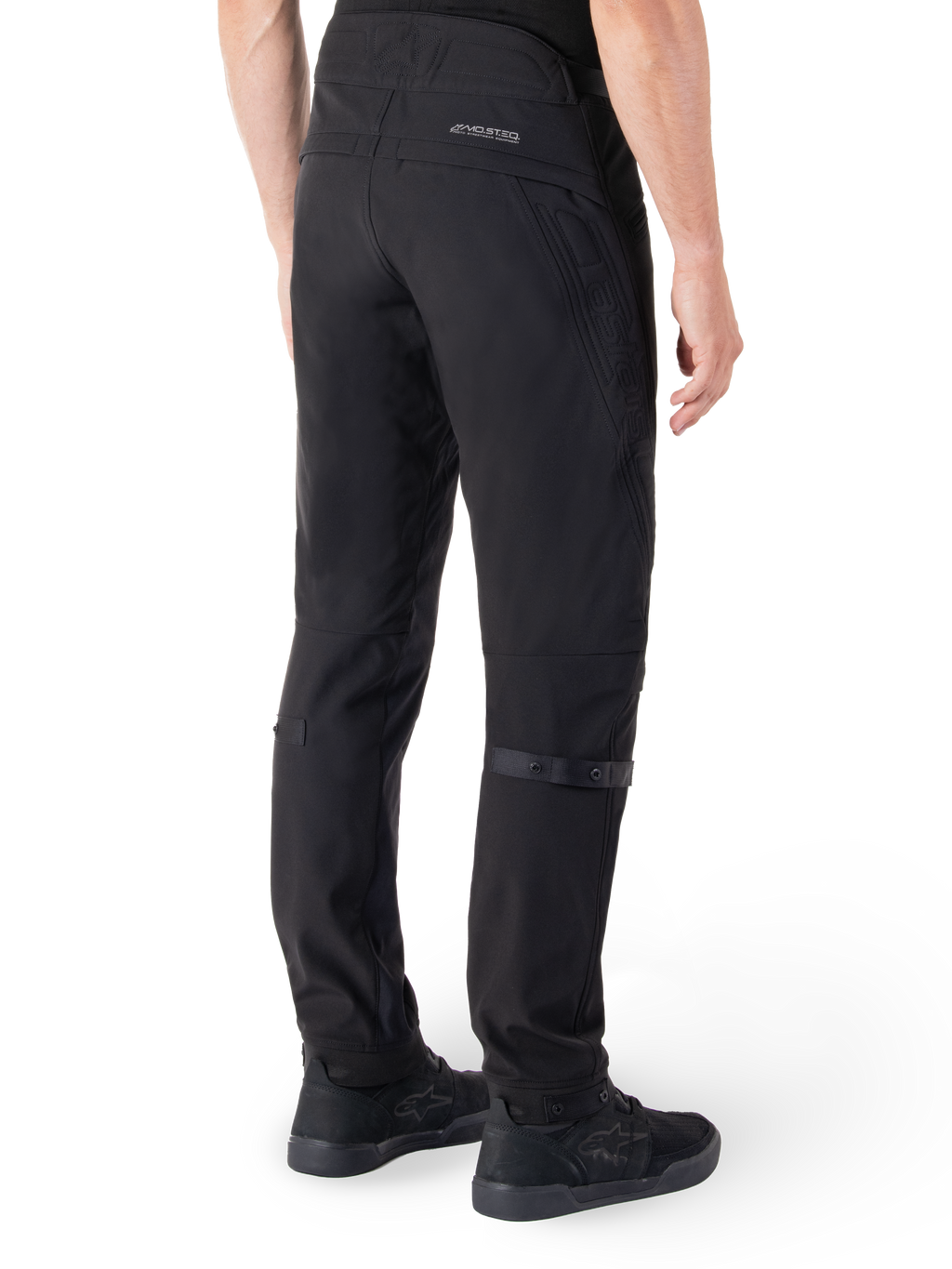Alpinestars Alden bukser, urbane motorcykelbukser, sort, set bagfra viser teknisk softshell-stof med quiltede detaljer, MO.ST.EQ. reflekterende branding på bagstykket og justerbare lægstropper, kombineret med sorte køresko