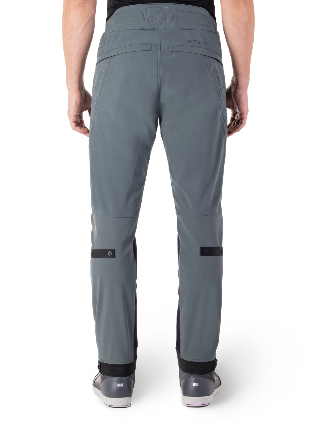 Alpinestars Alden bukser, Urban Gray, set bagfra af urbane motorcykelbukser til mænd, slim fit under knæet med sorte justeringsstropper på læggen, højtaljet design med MO.ST.EQ.-ordmærke på bagstykket, båret med grå køre sko