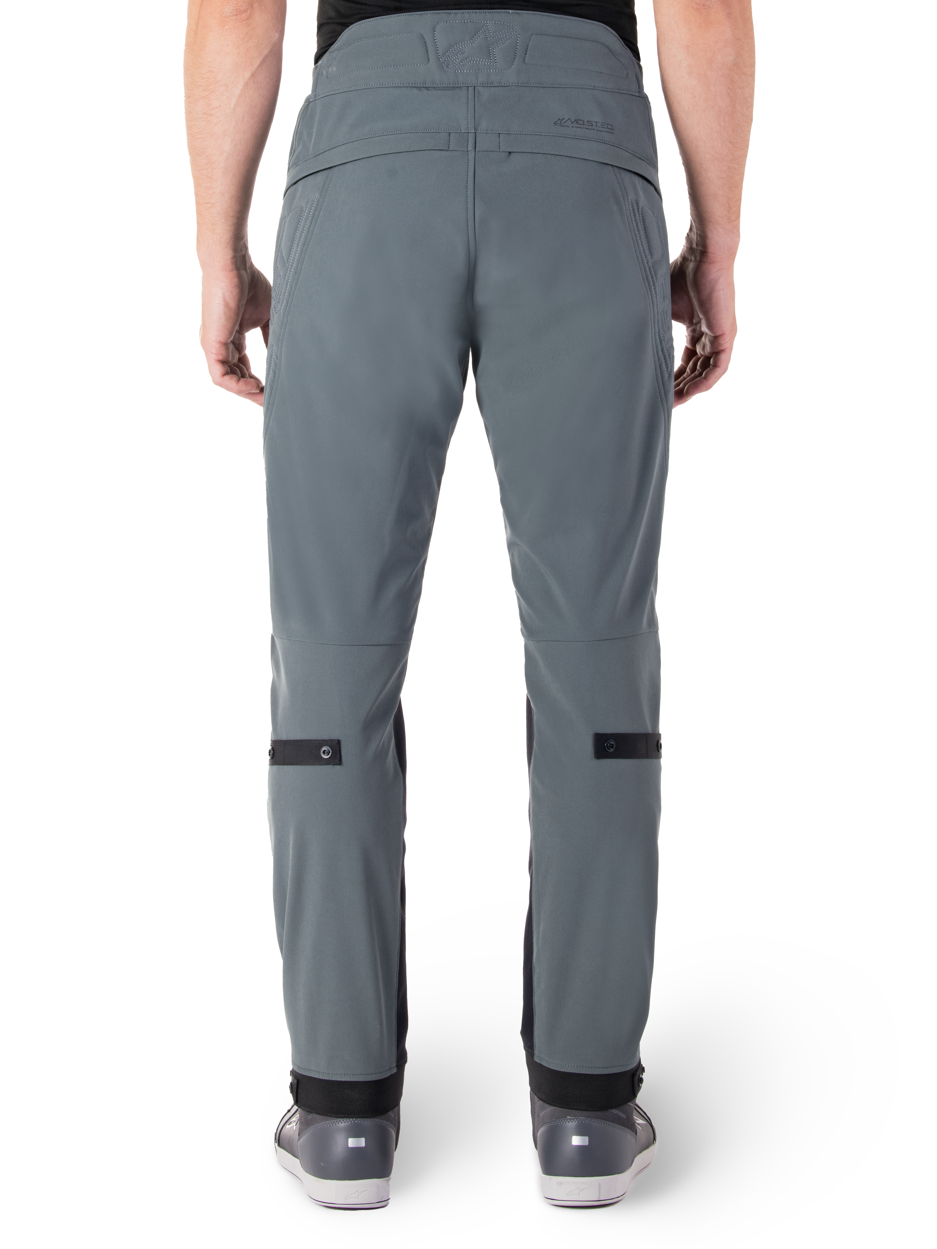 Alpinestars Alden bukser, Urban Gray, set bagfra af urbane motorcykelbukser til mænd, slim fit under knæet med sorte justeringsstropper på læggen, højtaljet design med MO.ST.EQ.-ordmærke på bagstykket, båret med grå køre sko