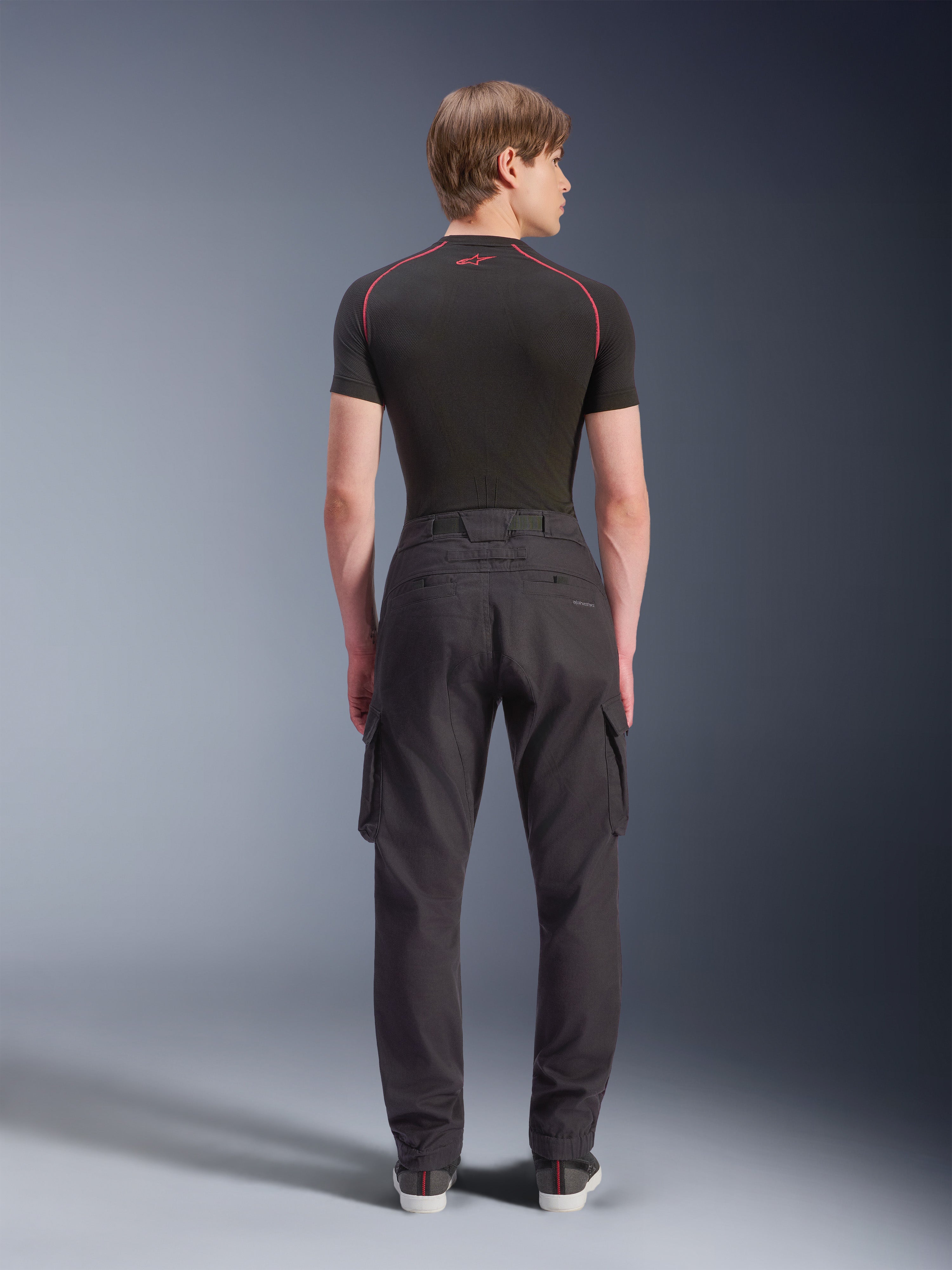 Alpinestars Flex-AST Cargo Pants - Short, sorte urbane motorcykelbukser set bagfra, med cargolommer på siderne og elastiske sømme, båret med et sort kortærmet basislag med røde kontrastsyninger