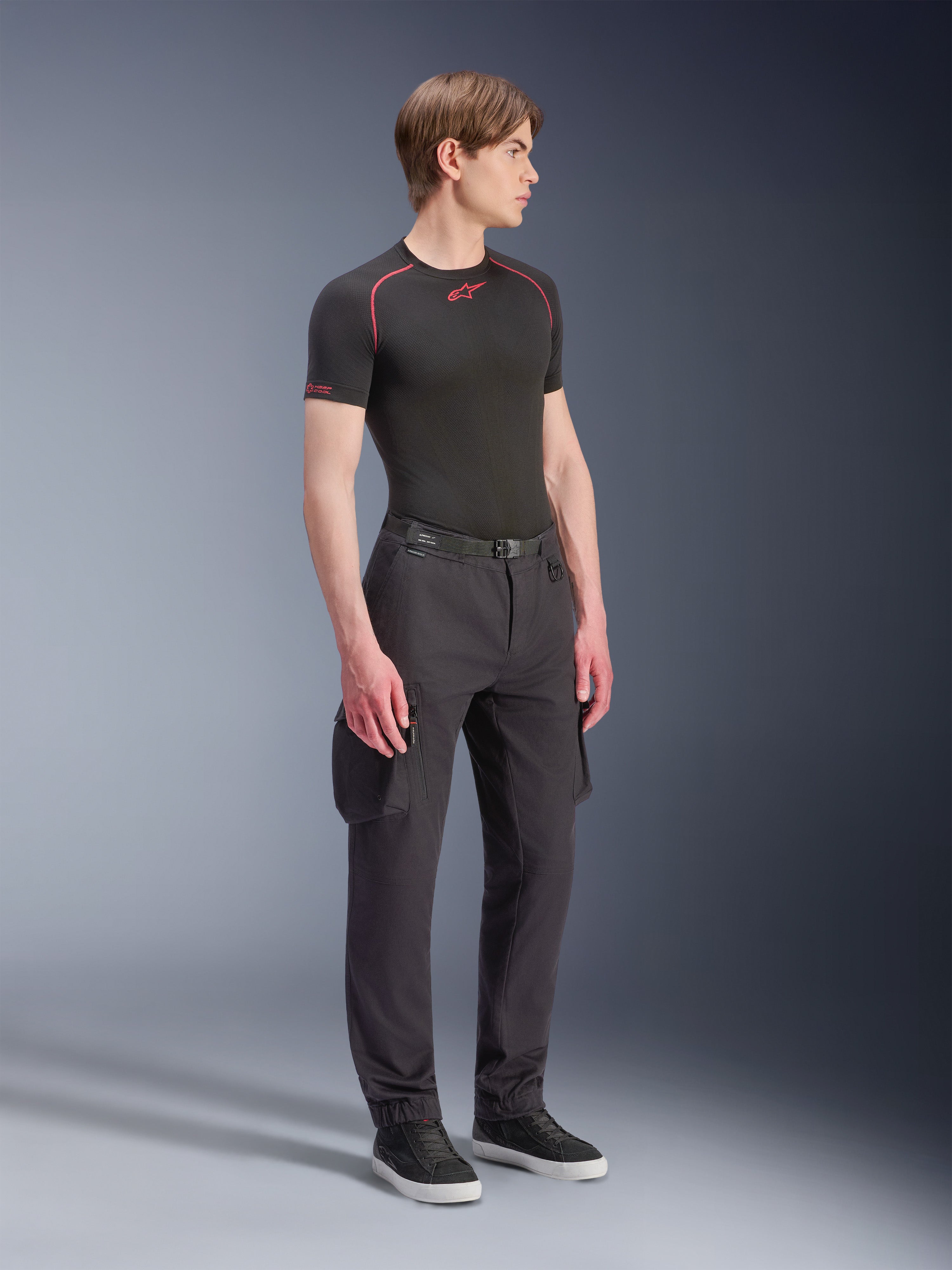 Alpinestars Flex-AST Cargo bukser, sort, urbane motorcykelbukser med cargolommer og elastiske kanter, båret af en model med sort kortærmet base layer og sneakers, moderne design med smalle ben