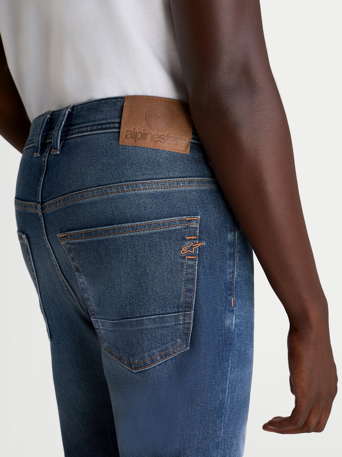 Alpinestars Flex-AST 8 Denim Pants, men's urban motorcycle riding jeans, medium blue, rear view showing leather back patch, contrast stitching, and embroidered Astar logo on the pocket worn by a model