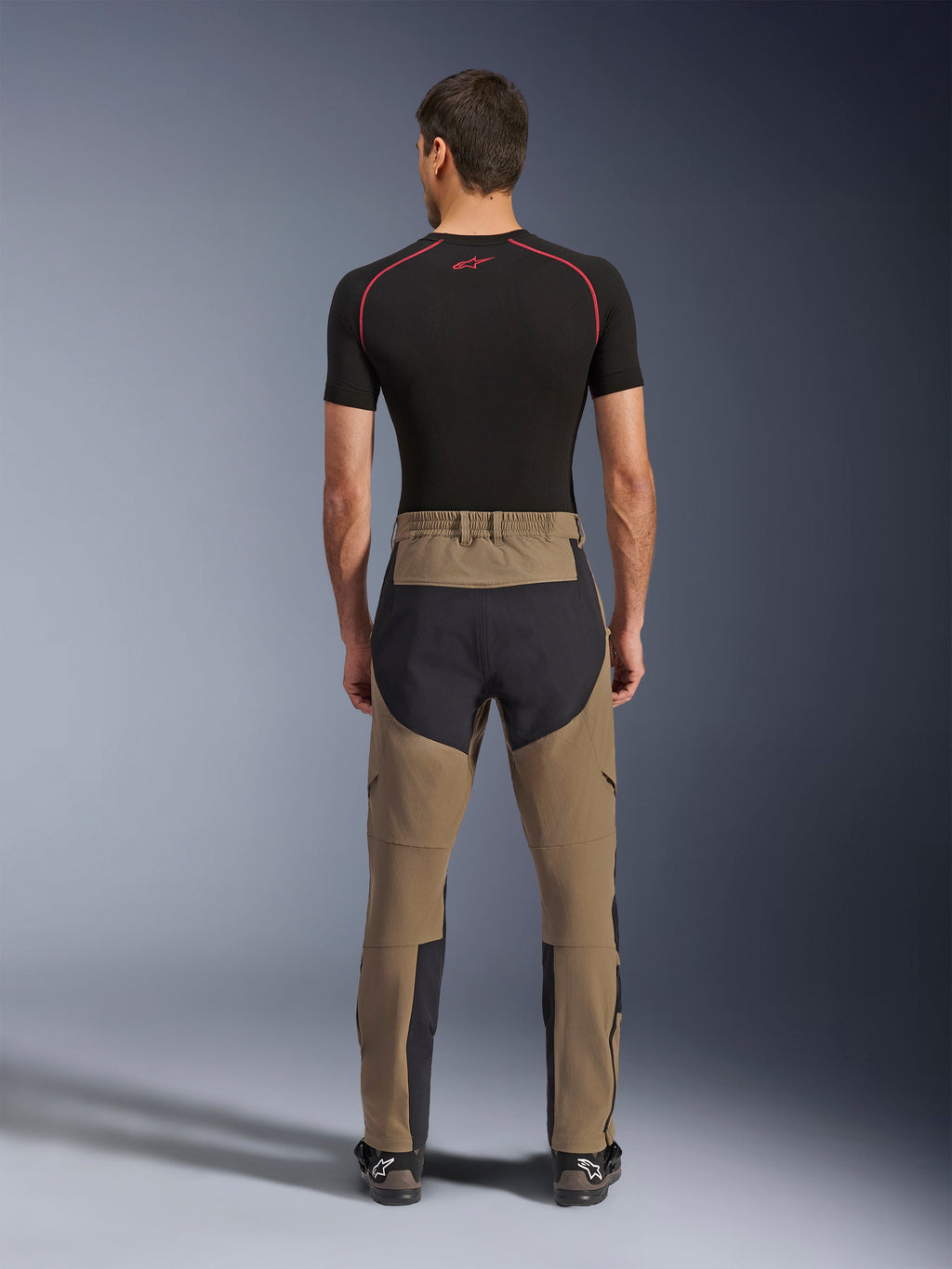 Alpinestars Flex-AST Explorer bukser, Walnut Black, set bagfra på model, med forstærket sort sæde og brunt stræktekstil, kombineret med sort baselayer og tekniske motorcykelstøvler, slidstærkt adventure-køreudstyr