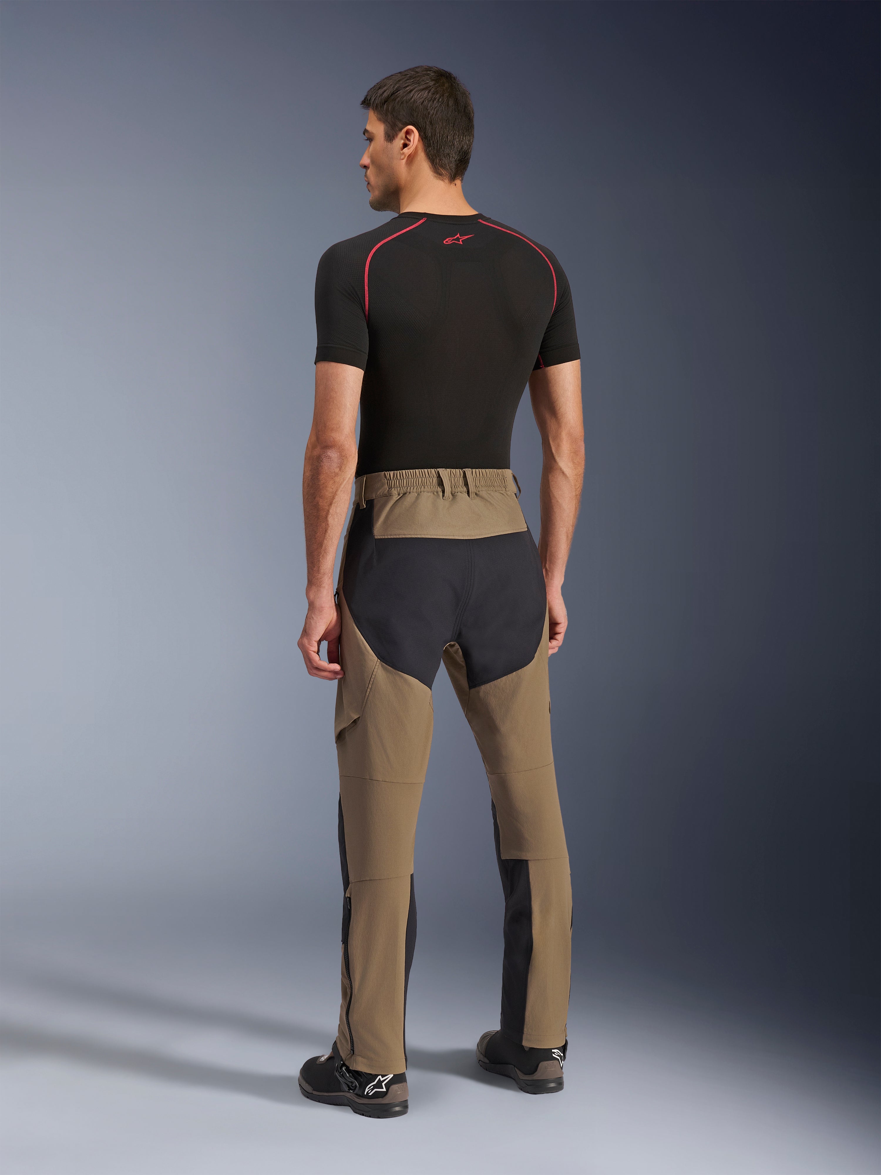 Alpinestars Flex-AST Explorer bukser, adventure-motorcykelbukser, Walnut Black, set bagfra på model, sorte ripstop-paneler på sæde og ben, strækbar tekstilkonstruktion, lange lynlåse på underbenene til adventure touring