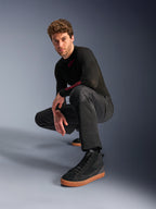 Alpinestars C-1 Air bukser, urban motorcykelbukser, sort, model der sidder på hug i et studiemiljø, båret med en sort langærmet overdel og sorte sneakers med brune såler, med åndbare mesh-paneler og en moderne urban stil