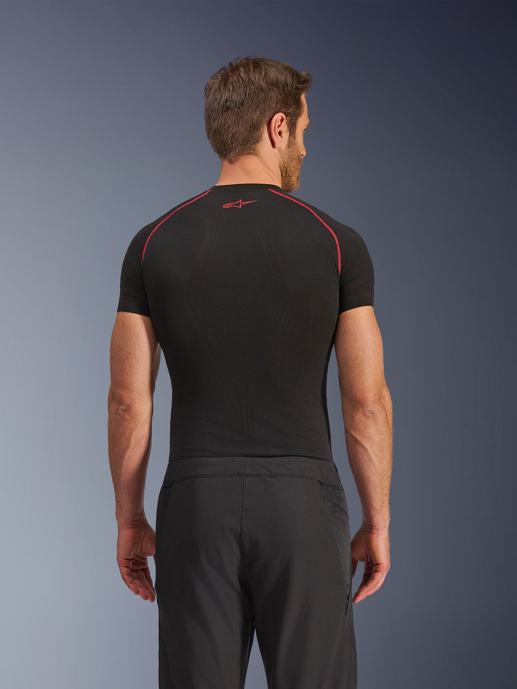 Alpinestars Aeroshell Airflow bukser, set bagfra, sorte, letvægts softshell-konstruktion med integrerede mesh-sidepaneler, kombineret med et sort basislag med røde kontrastsyninger, sportsligt motorcykeludstyr