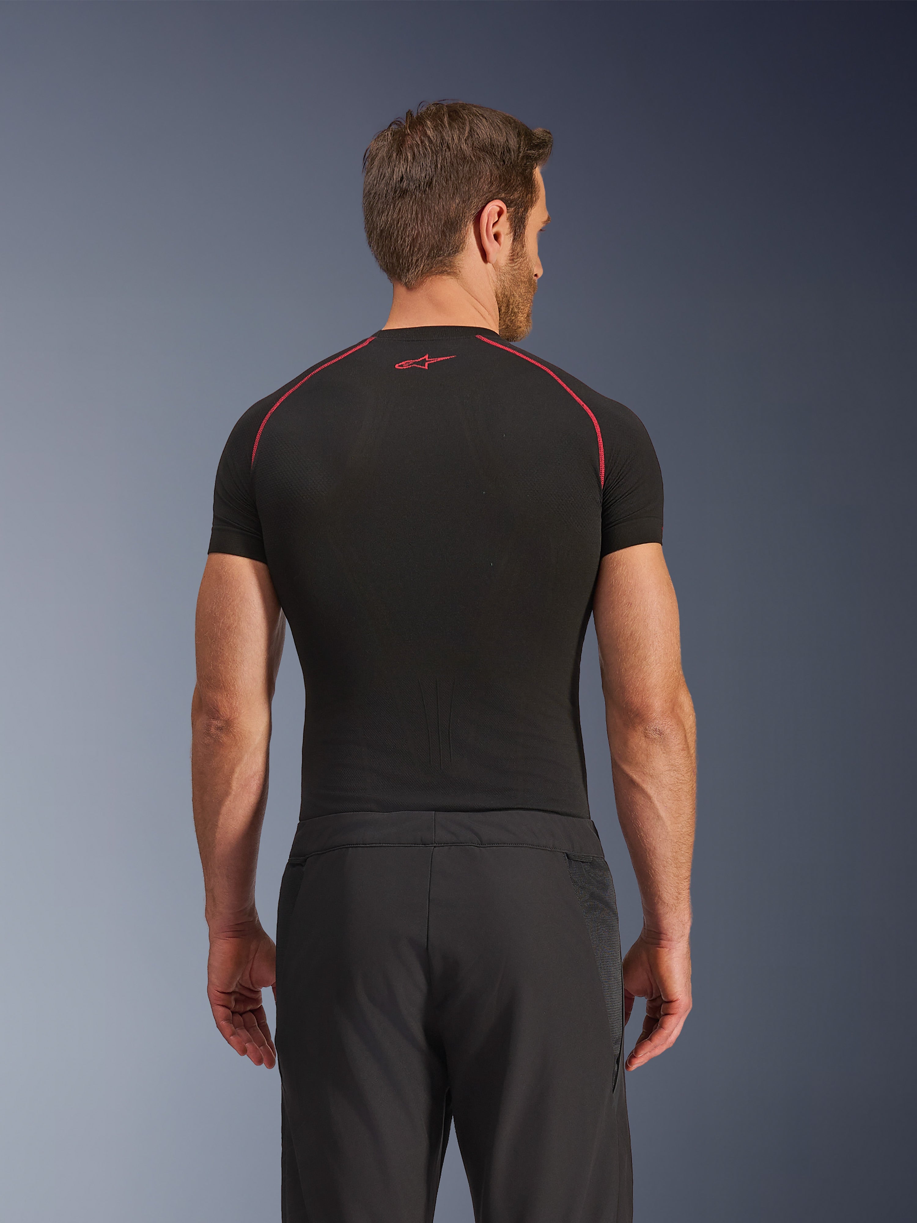 Alpinestars Aeroshell Airflow bukser, set bagfra, sorte, letvægts softshell-konstruktion med integrerede mesh-sidepaneler, kombineret med et sort basislag med røde kontrastsyninger, sportsligt motorcykeludstyr