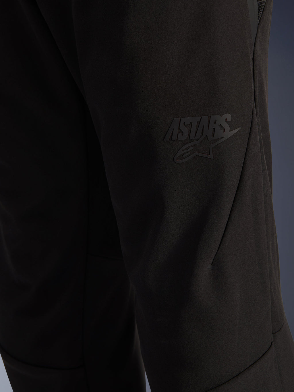 Alpinestars Aeroshell Airflow bukser, sorte motorcykelbukser, nærbillede af lårområdet med et ophøjet sort ASTARS-logo, letvægts stræk-softshell-materiale med ergonomisk sømdesign