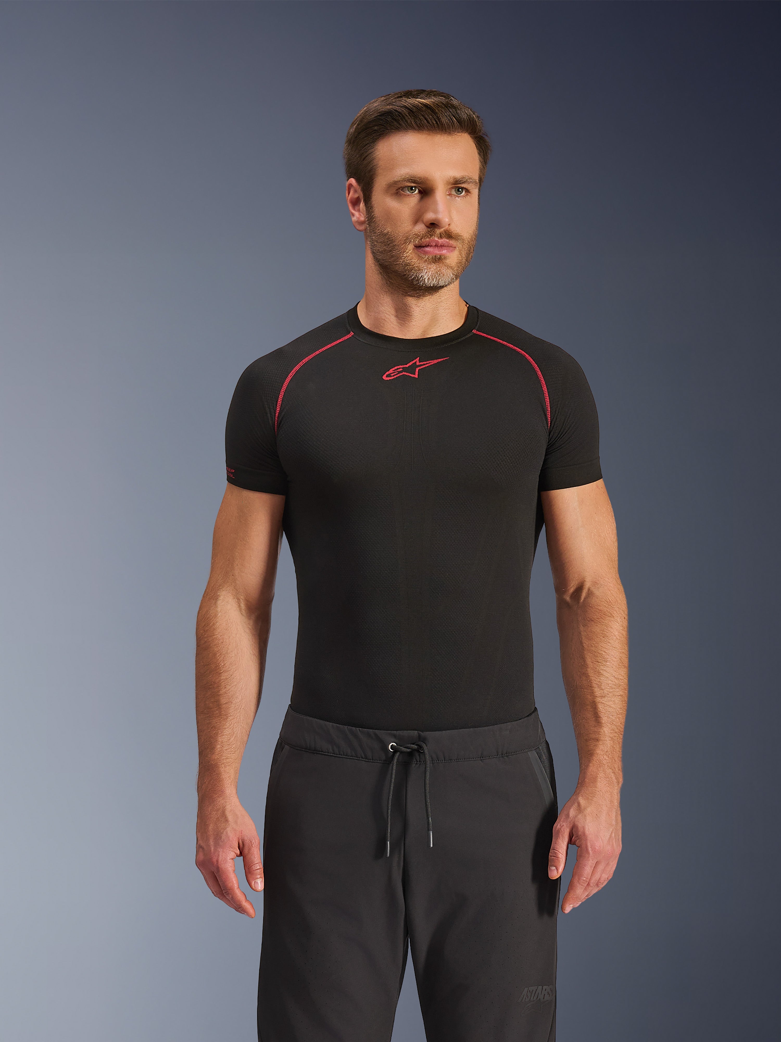 Alpinestars Aeroshell Airflow bukser, sorte motorcykelbukser, letvægts softshell-tekstil, med løbesnor i taljen og laserperforeret ventilation, båret sammen med en sort Alpinestars base layer-trøje