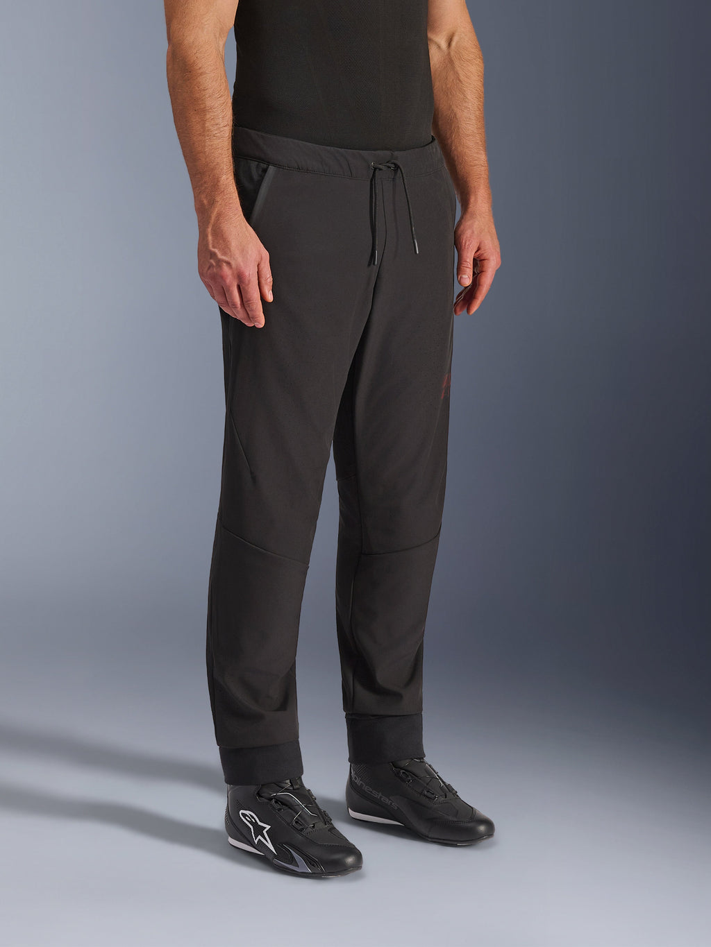 Alpinestars Aeroshell Airflow bukser, sorte motorcykelbukser, båret af model med sorte køresko, med snøre i taljen, ankelmanchetter og laserperforeret softshell-materiale for maksimal ventilation