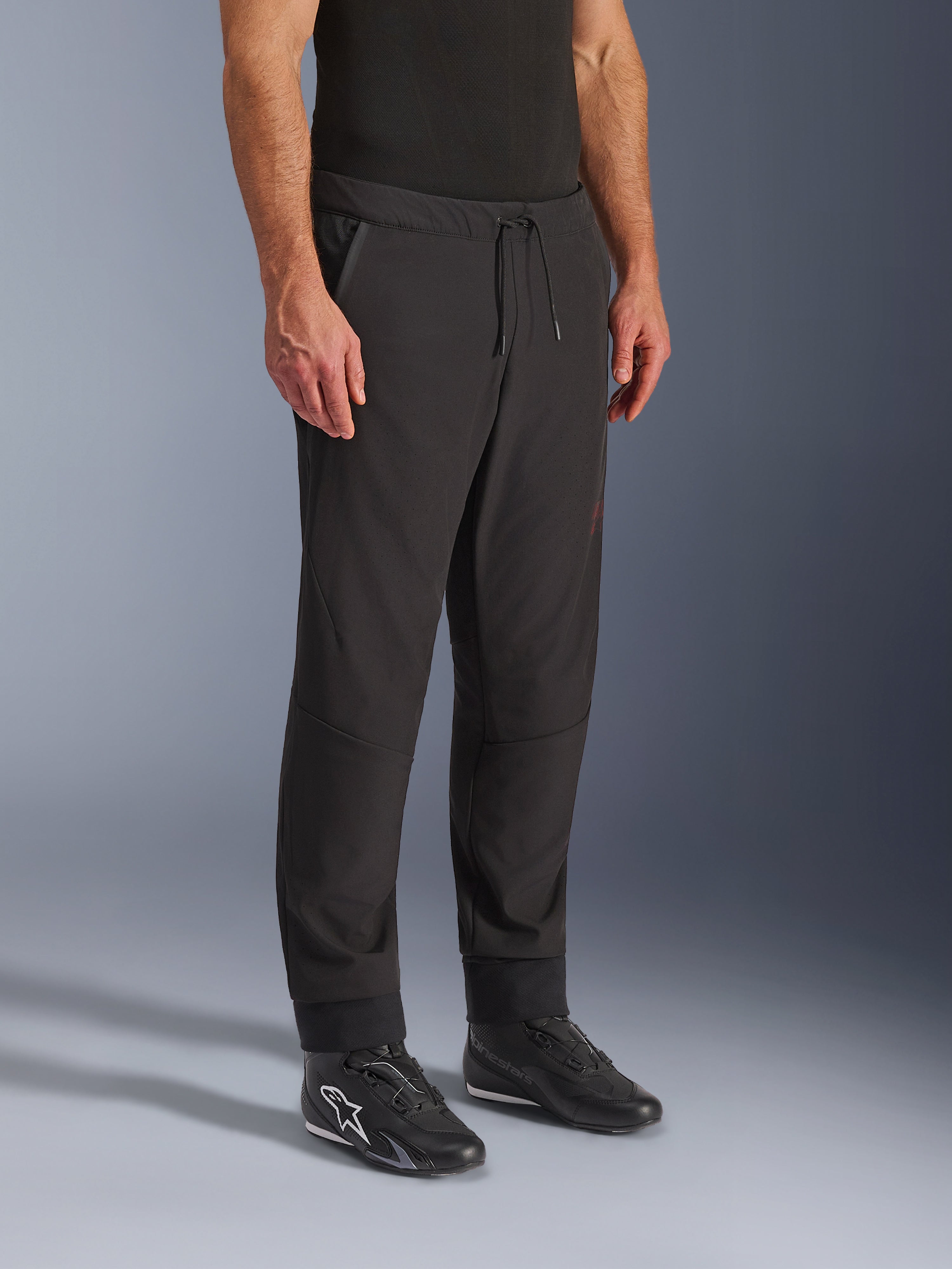 Alpinestars Aeroshell Airflow bukser, sorte motorcykelbukser, båret af model med sorte køresko, med snøre i taljen, ankelmanchetter og laserperforeret softshell-materiale for maksimal ventilation
