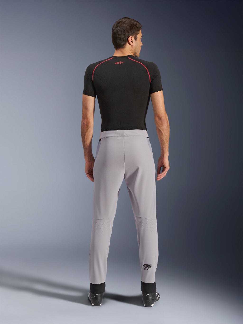 Alpinestars Aeroshell Airflow bukser, Mid Gray, set bagfra med laserperforerede zoner på læggene, letvægts strækbar softshell-konstruktion, båret med sort kortærmet trøje og motorcykelstøvler, sport-fit design til kørsel i varmt vejr