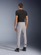 Set bagfra af en model iført Alpinestars Aeroshell Airflow bukser i Mid Gray, kombineret med en sort baselayer-trøje og sorte sko, hvilket fremhæver de laserperforerede zoner på læggene og den atletiske sportspasform.