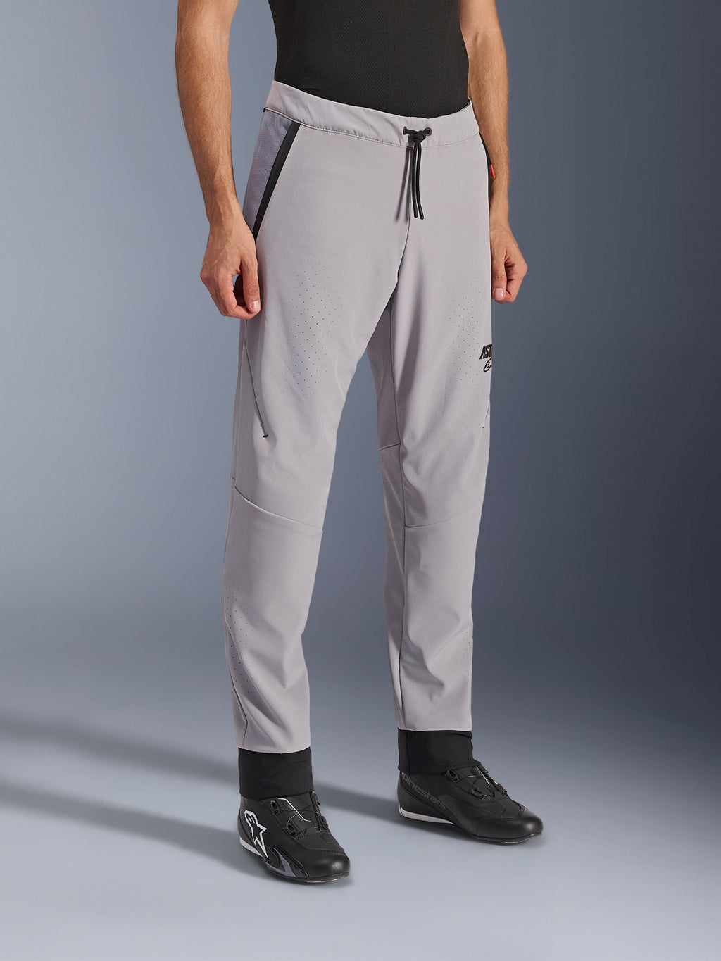 Alpinestars Aeroshell Airflow bukser, mellemgrå, letvægts motorcykelbukser med laserperforerede ventilationszoner på lår og skinneben, med elastisk linning med snoretræk og en tætsiddende sport-pasform, vist på en model iført sorte køresko.